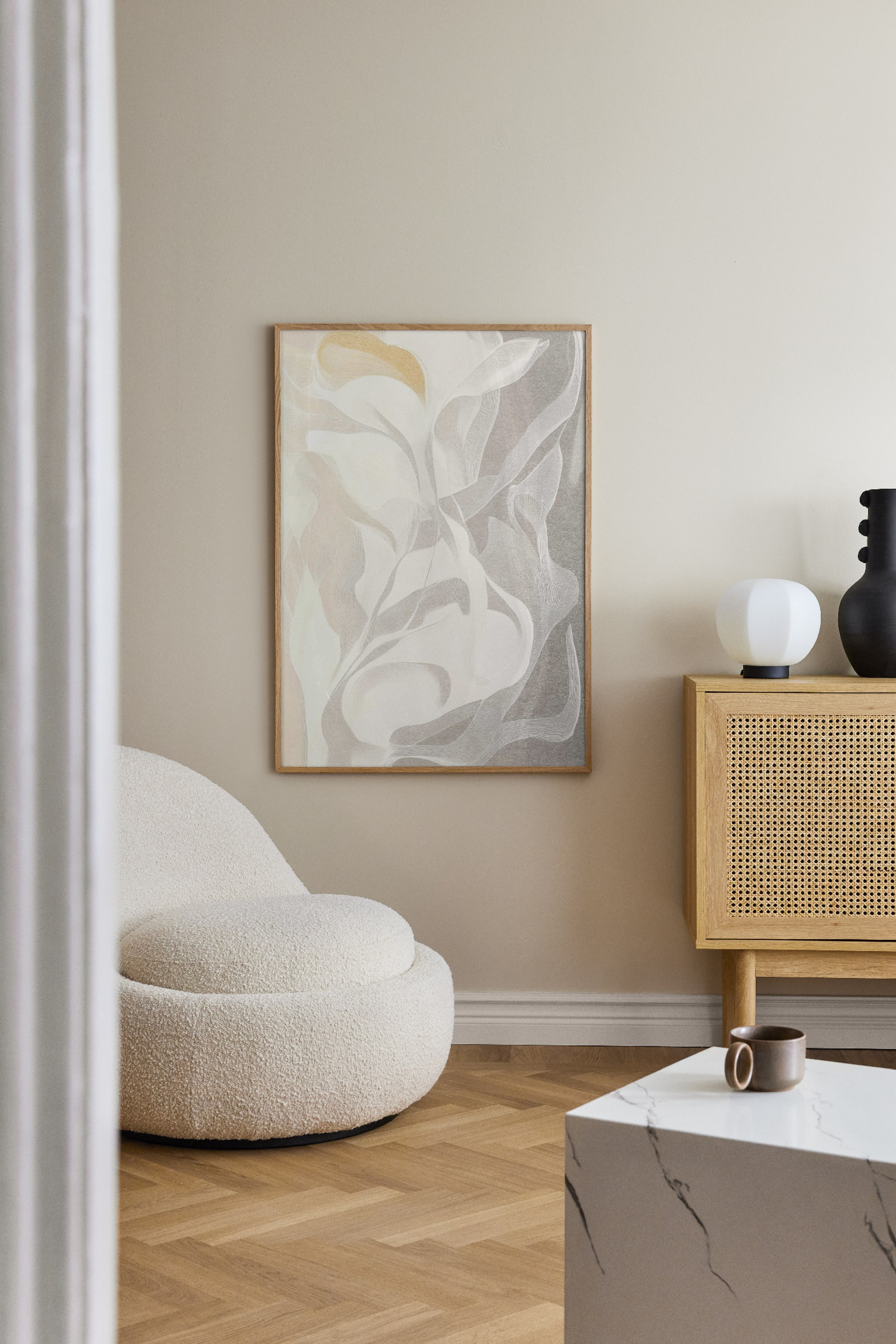 Ver imagen más grande: Una obra de arte rectangular cuelga en vertical en una pared, orientada directamente hacia delante. Presenta una composición abstracta de formas orgánicas y fluidas en tonos blancos, gris claro y dorado suave, enmarcada en un marco de madera clara.