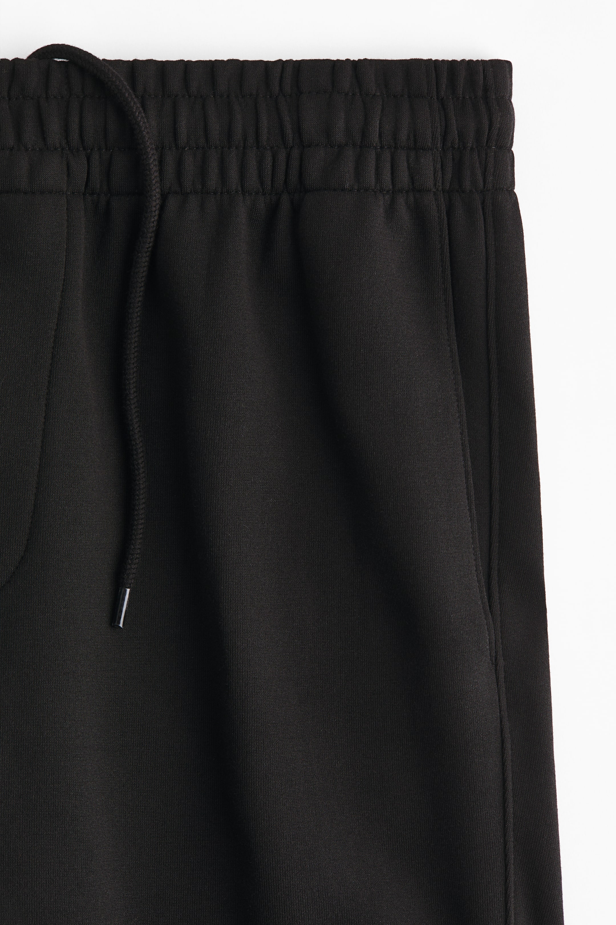 View larger image: Black sweatpants are featuring an elasticated waistband with gathers, a black drawstring with silver tips emerging from the front, and a side pocket with a visible seam.
