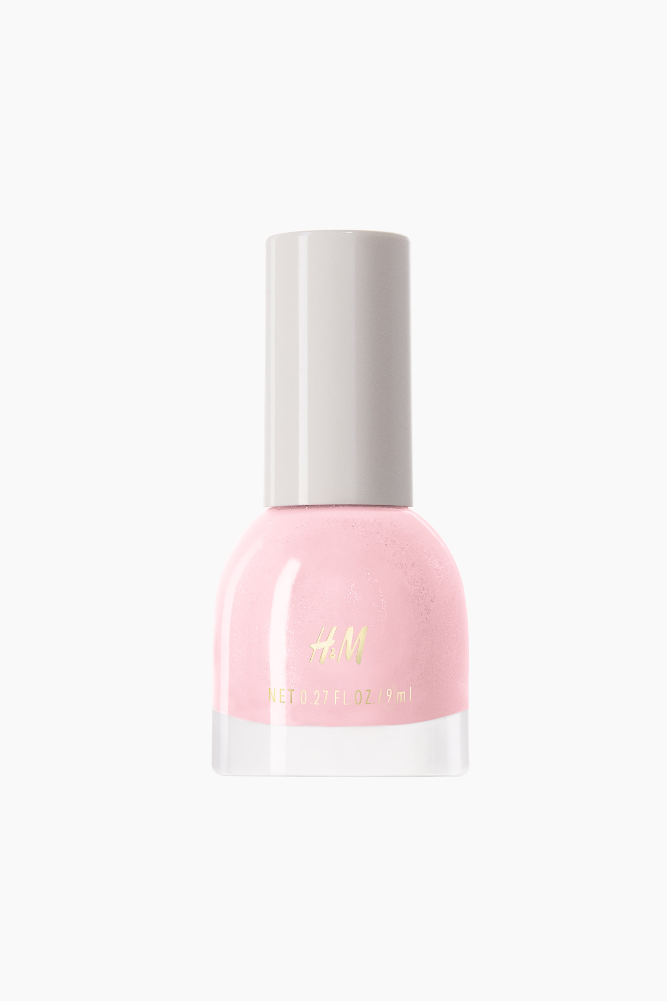 View larger image: A light pink nail polish bottle is standing front-facing, featuring a rounded glass body filled with pink polish and a clear glass base. An opaque light grey cylindrical cap is topping the bottle, which is displaying gold H&M branding and net volume.