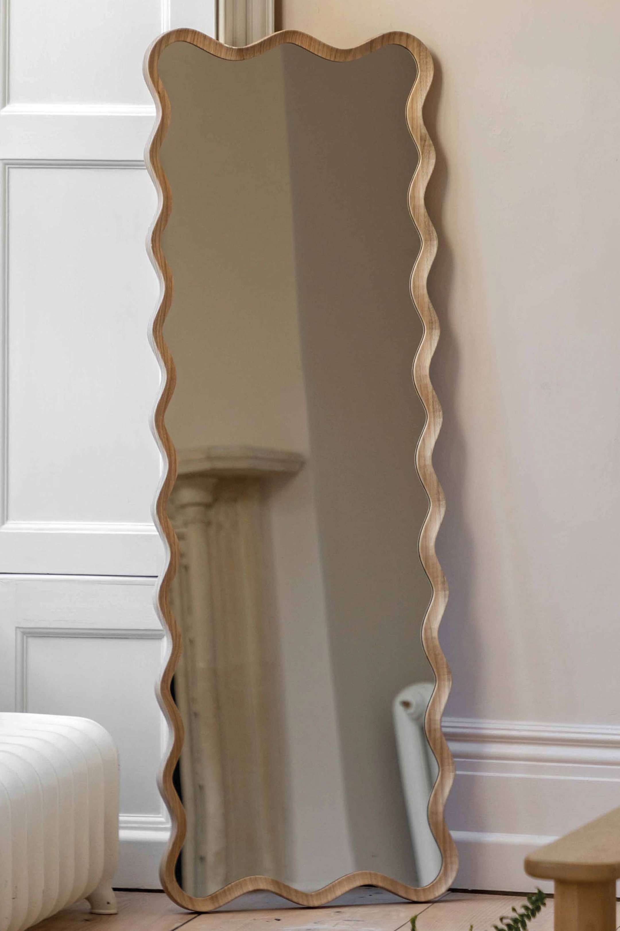 View larger image: A full-length mirror stands upright, featuring a light wood frame with a wavy, undulating edge.