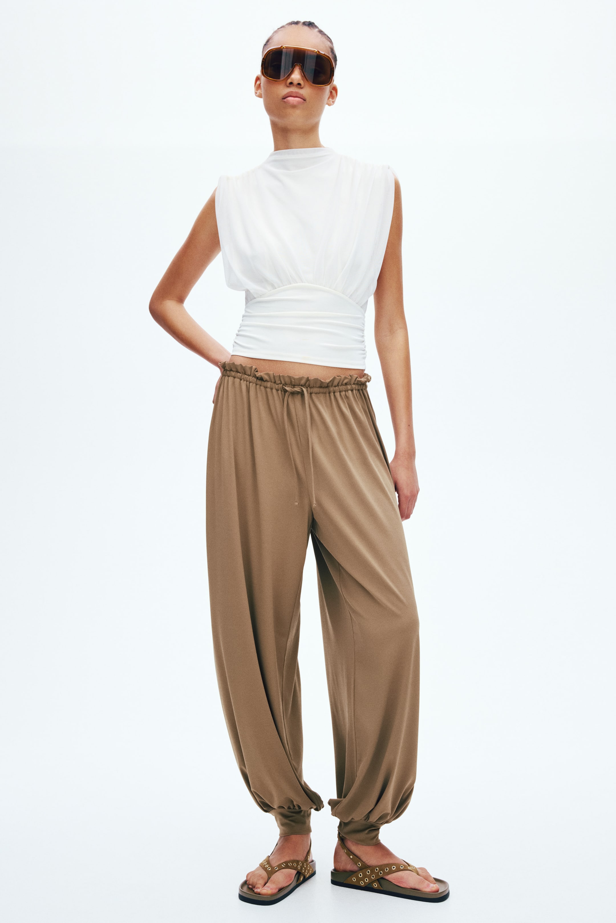 הצגת תמונה גדולה יותר: המכנסיים החומים כוללים גזרה נינוחה, מותן גבוהה עם גומי וקשירה, וסיומות מכווצות בקרסוליים.