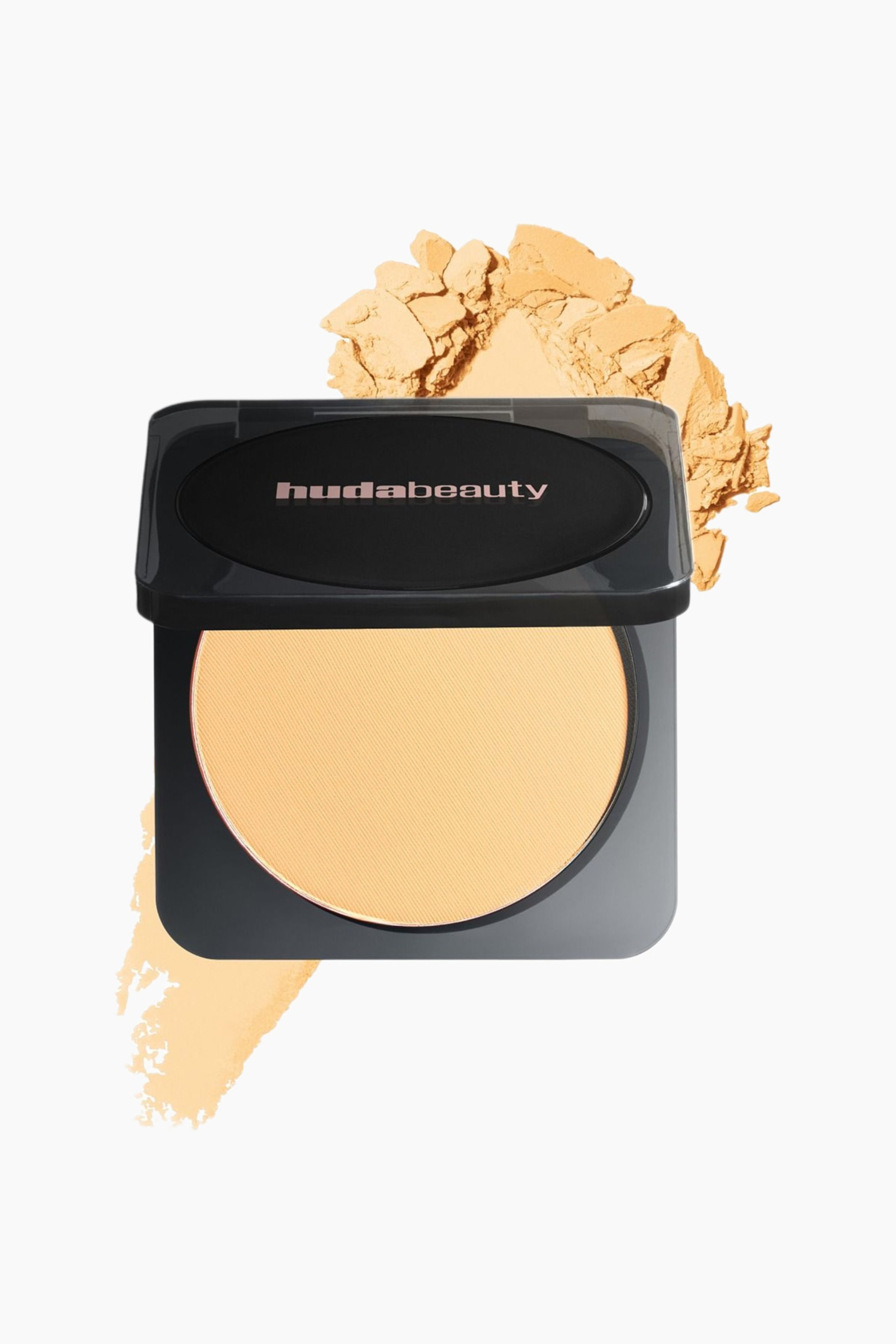 Vis større bilde: En svart Huda Beauty pressed powder compact er åpen og viser en sirkulær pan med lysgult pudder. Løst pudder ligger spredt bak og til venstre for compacten, og en powder swatch er synlig nedenfor.