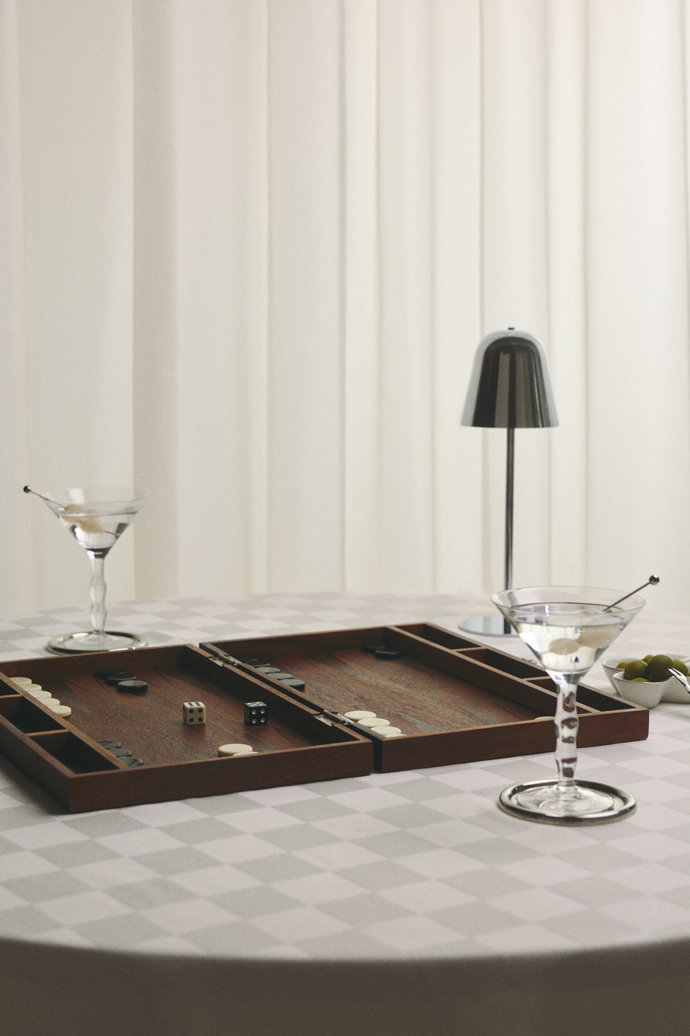 A closed wooden backgammon case is resting in a front-facing position, showcasing its rich brown woodgrain finish. The top lid features inlaid concentric rectangular lines, while a silver metal clasp secures the front centre, and the word "BACKGAMMON" appears on the bottom right edge.