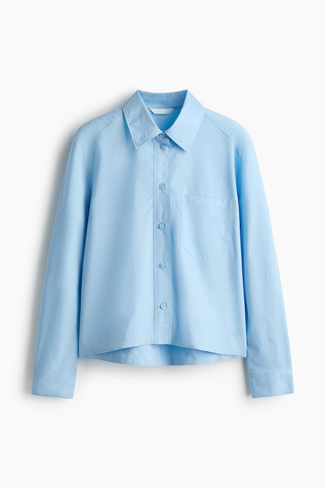 A light blue shirt is featuring a pointed collar, a full button-front placket with matching light blue buttons, and a patch pocket on the left chest. It is designed with long sleeves and a subtly curved hem. - 1