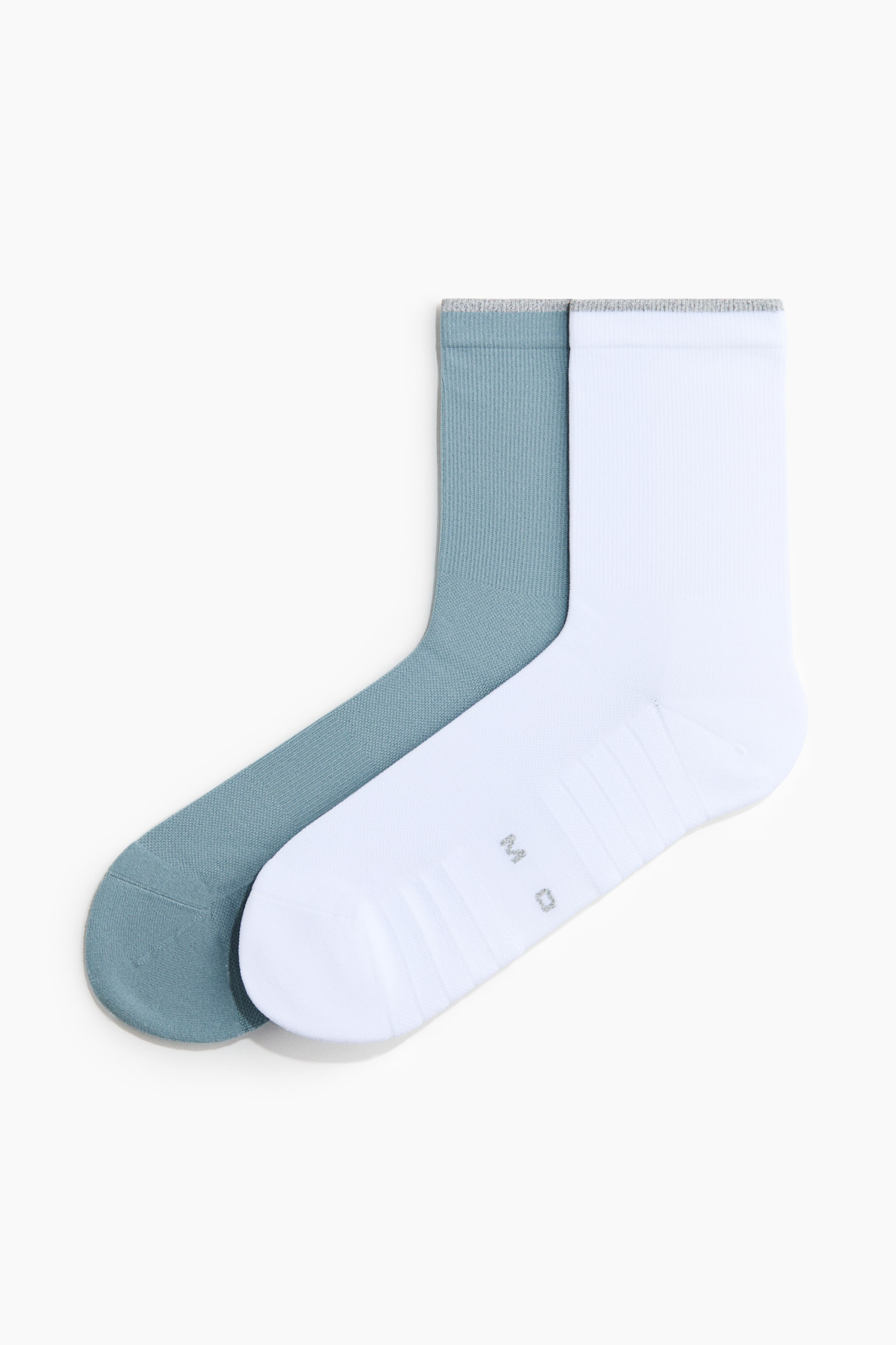 Voir une image plus grande: Une paire de chaussettes est posée à plat et se chevauche. Une chaussette est blanche avec les lettres "M D" grises sur le dessus du pied, et l'autre est d'un bleu sarcelle discret. Les deux chaussettes présentent des poignets côtelés gris et des sections texturées sur le pied et le talon.