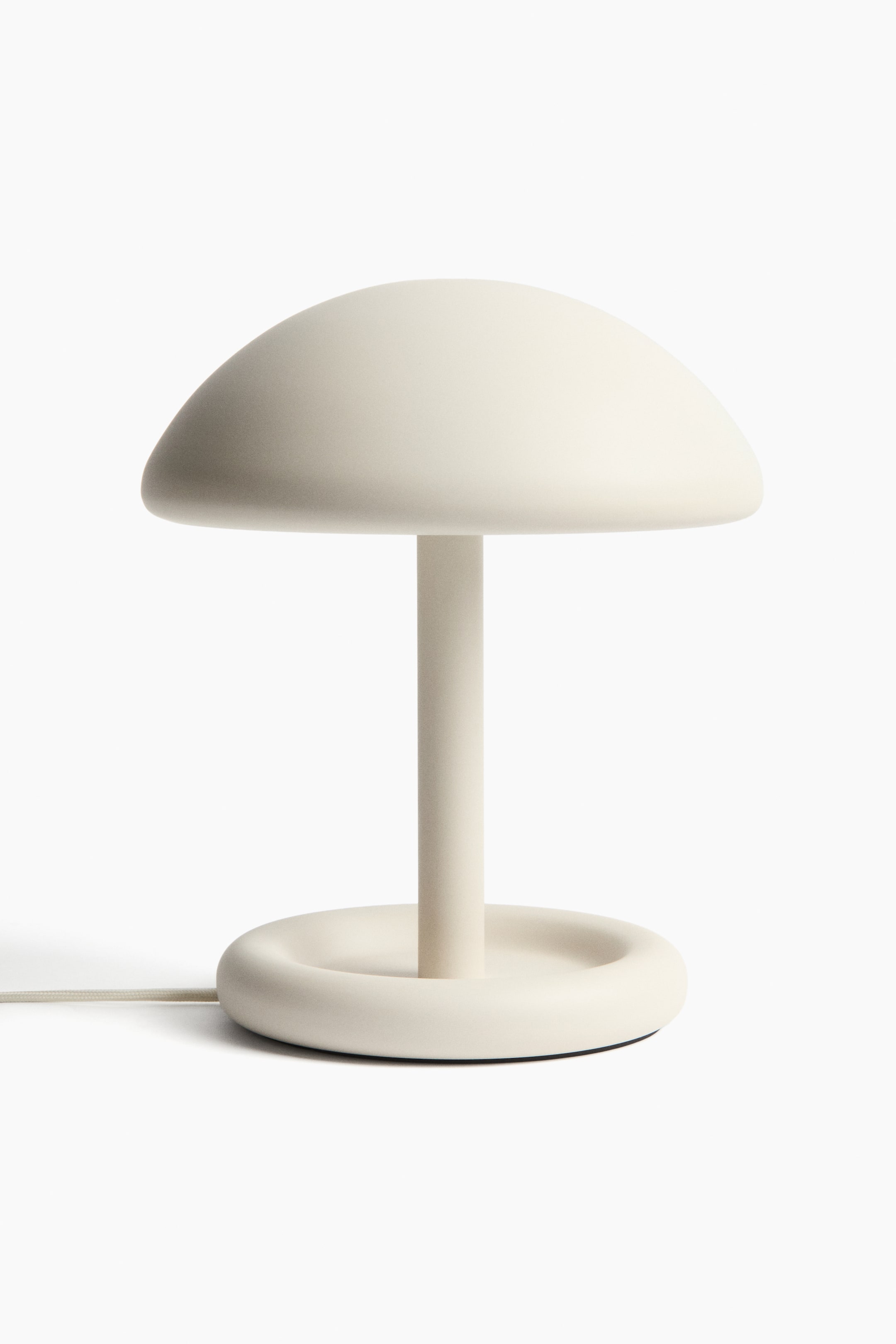 Größeres Bild ansehen: Eine cremefarbene Lampe mit einer abgerundeten Kuppelschirm, einem zylindrischen Stiel und einem kreisförmigen Sockel mit erhöhtem Rand, aus dessen Seite ein Stromkabel herausragt.