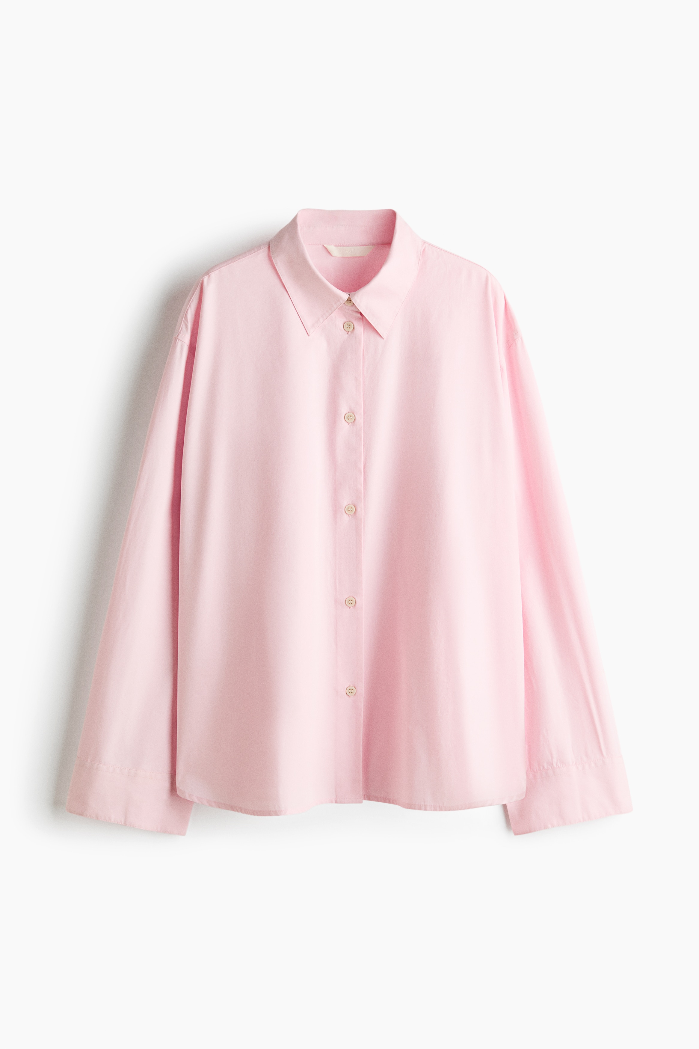A light pink, relaxed-fit shirt in a cotton weave is being worn by the model. The shirt features a pointed collar, dropped shoulders, long sleeves with button cuffs, and a partially open button-down front.