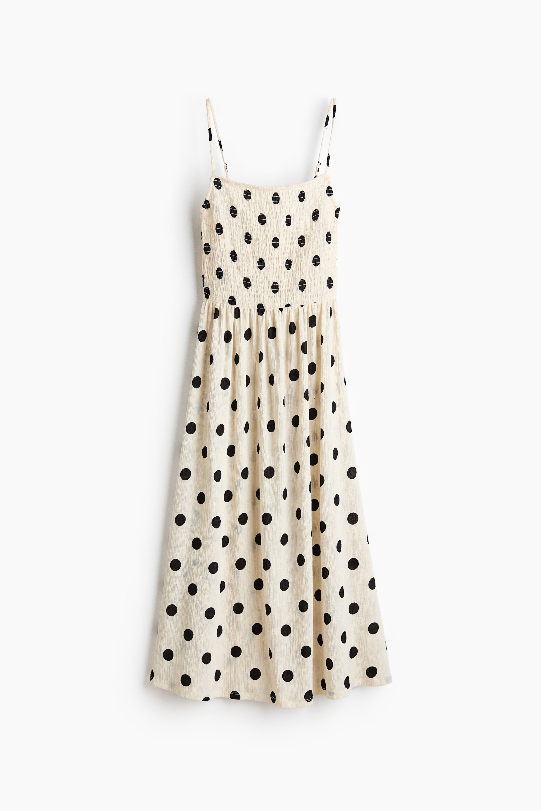 View larger image: A cream calf-length dress adorned with black polka dots showcases a crinkled jersey fabric. It is crafted with a smocked bodice, a square neckline, and adjustable spaghetti shoulder straps, culminating in a gathered seam at the waist and a flared skirt.