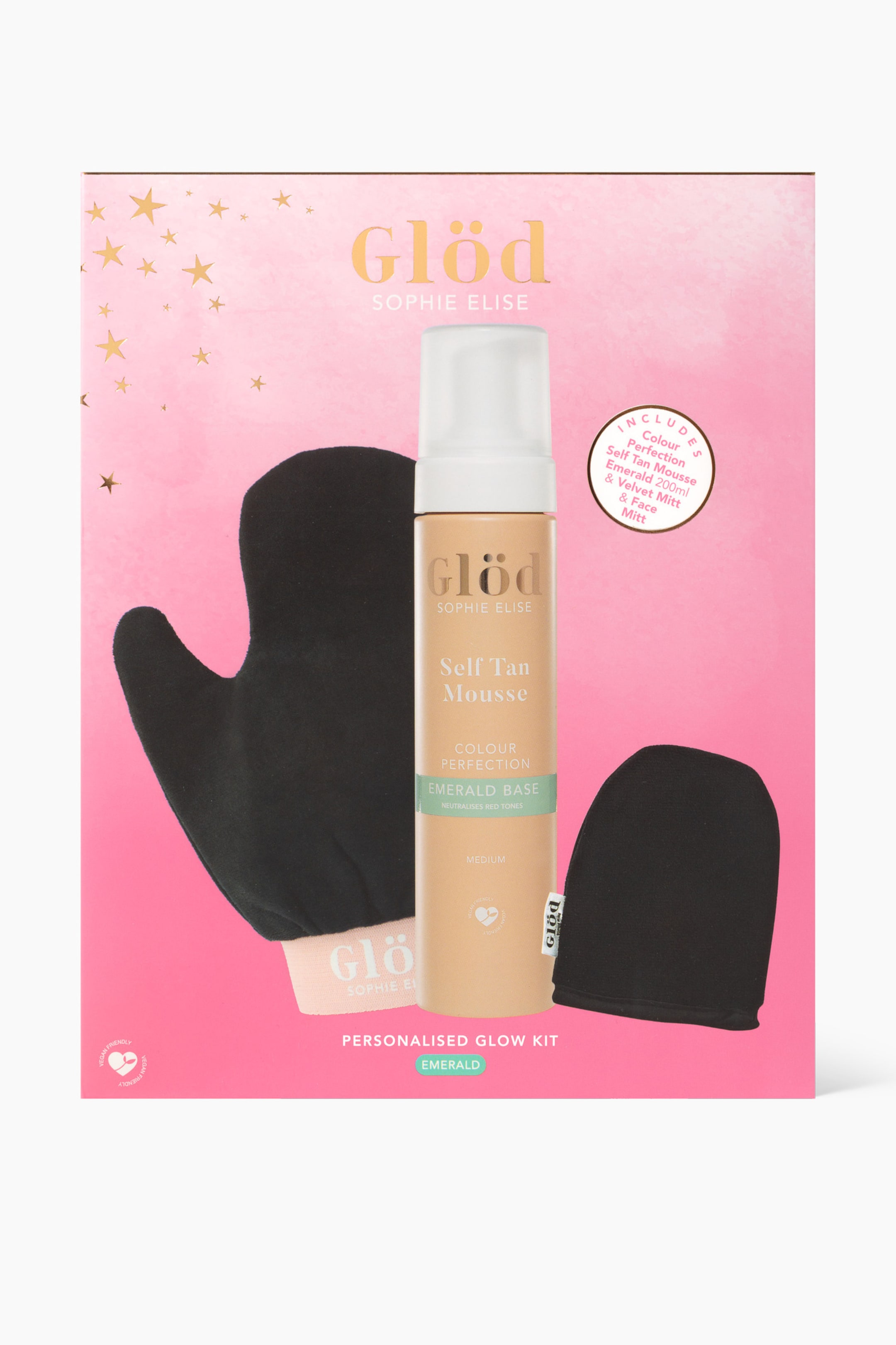 Vis større bilde: Et selvbruningssett presenteres rett forfra inne i en rosa eske med gullstjerneaksenter. Settet inneholder en beige selvbruningsmousseflaske med en hvit pumpe, en stor svart fløyelshanske med en merket mansjett, og en mindre svart fløyelshanske for ansiktet.