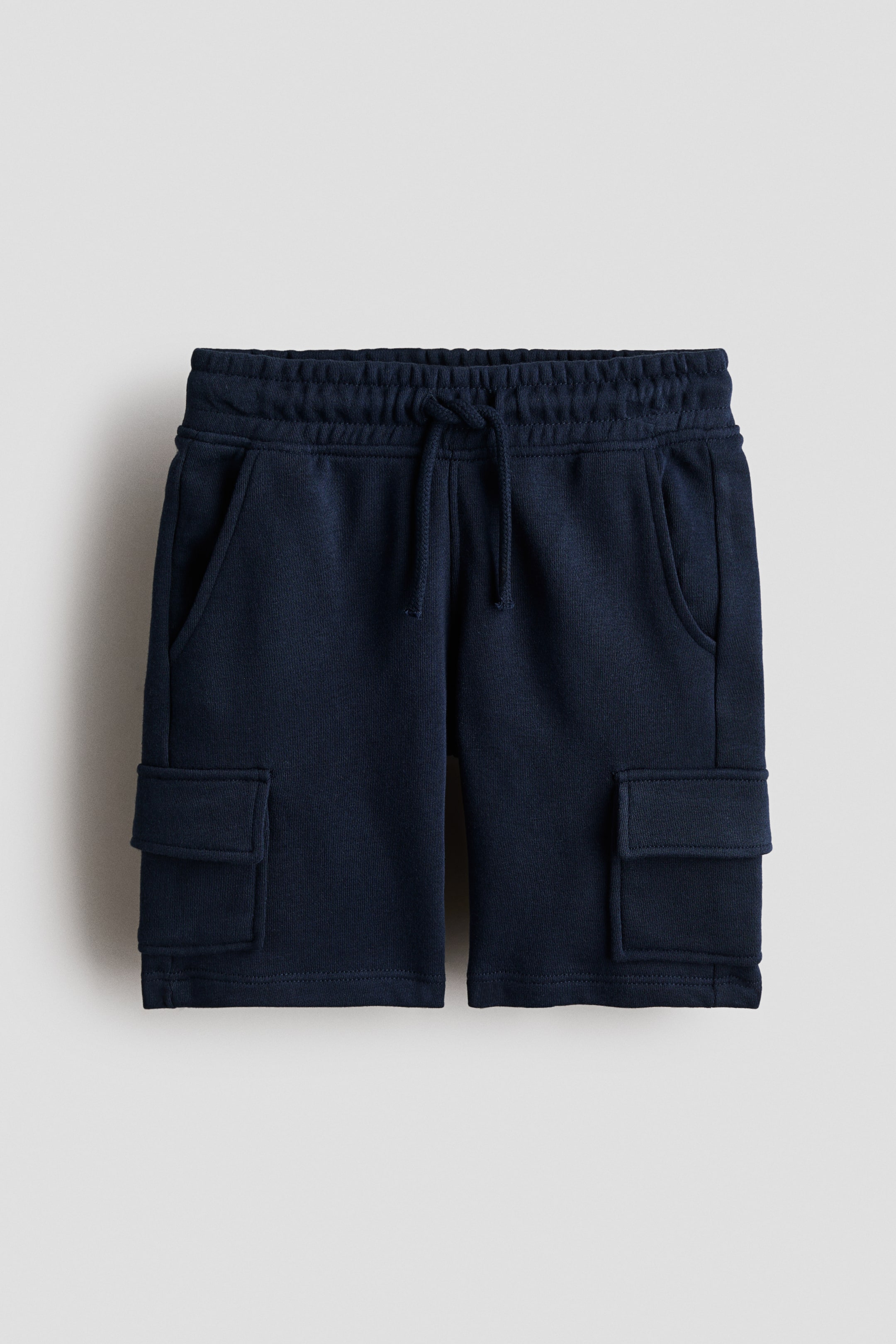 Agrandir l'image: Shorts cargo longueur genou en tissu de sweat-shirt bleu foncé, affichant leur DEVANT, avec une taille élastiquée à cordon de serrage, des poches latérales en biais et des poches à rabat sur les jambes.