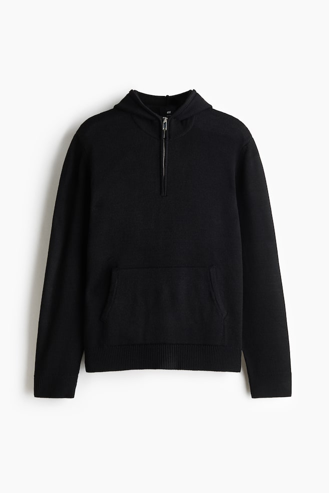 Una felpa con cappuccio nera lavorata a maglia è mostrata in vista frontale, mettendo in risalto la morbida texture della maglia, il cappuccio integrato e la chiusura half-zip color argento. Il capo a maniche lunghe presenta una tasca a marsupio sul davanti e un ampio bordo a coste. - 1