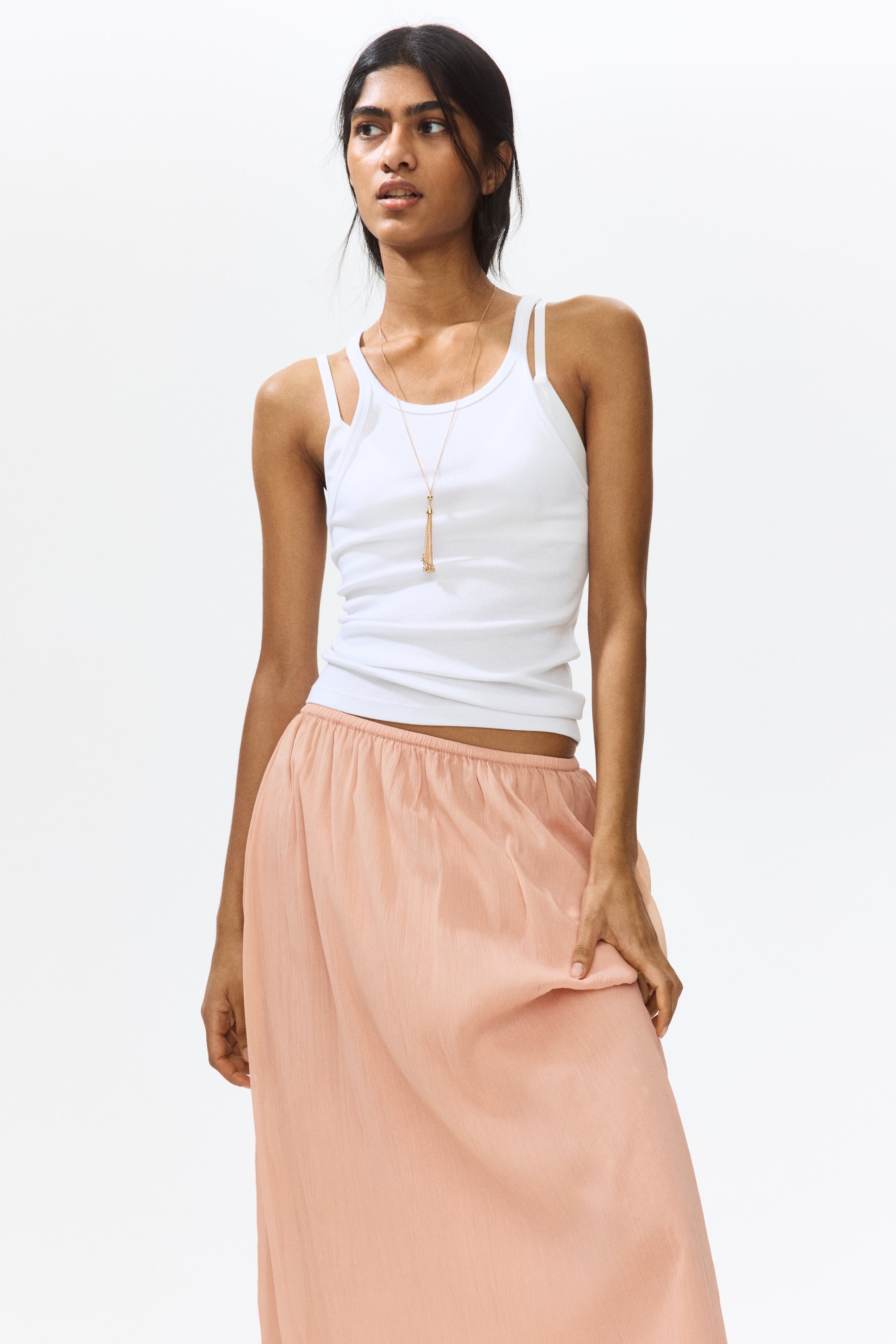 View larger image: The model is showcasing a calf-length skirt crafted from peach crinkled chiffon, featuring a covered elasticated waistband. She is gracefully holding a section of the skirt's fabric.