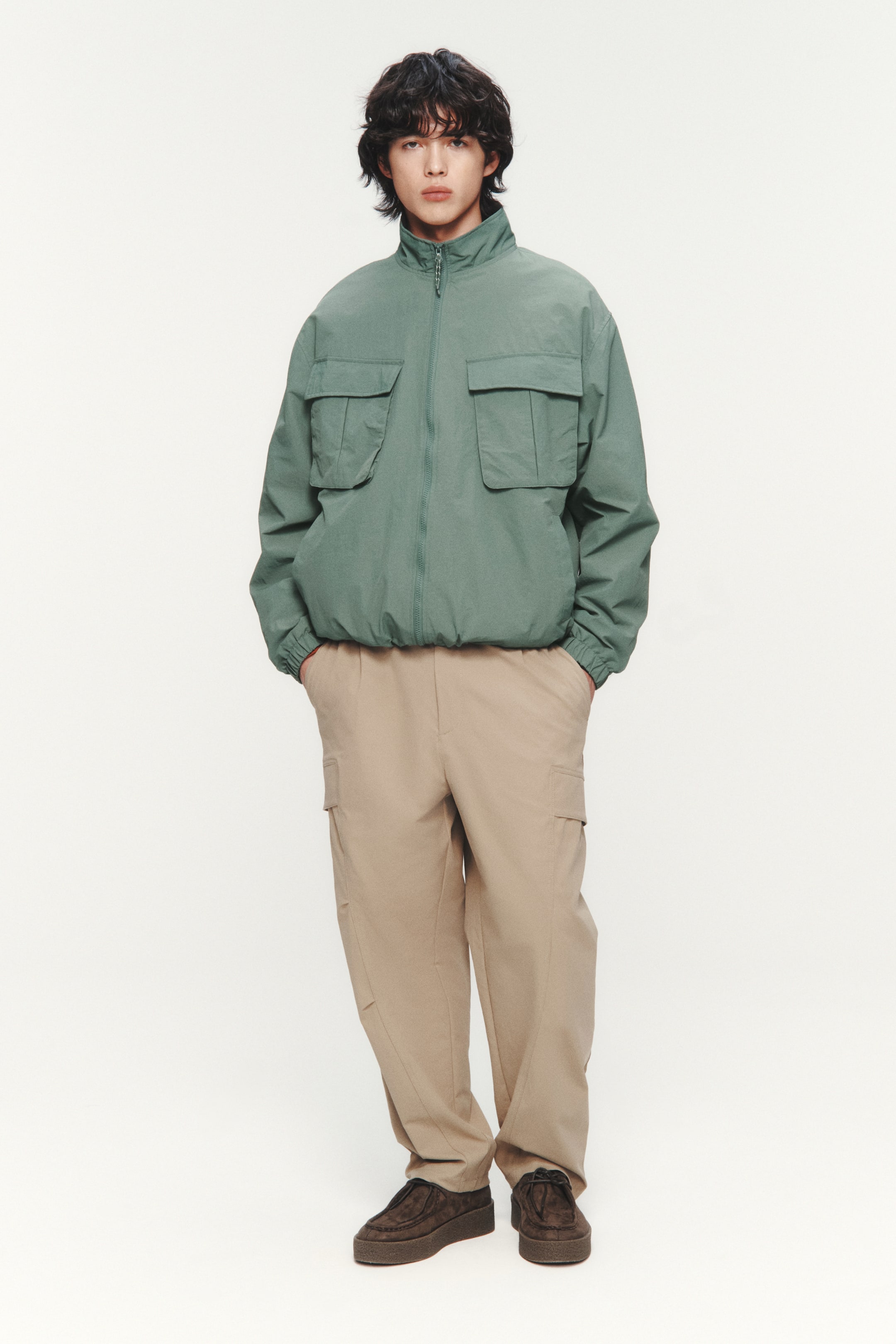 이미지 확대 보기: 녹색 봄버 재킷은 높은 스탠드 칼라와 전체 지퍼 업 프론트가 특징입니다. 가슴에 두 개의 큰 플랩 포켓이 있으며, 신축성 있는 커프스와 신축성 있는 밑단이 돋보입니다.