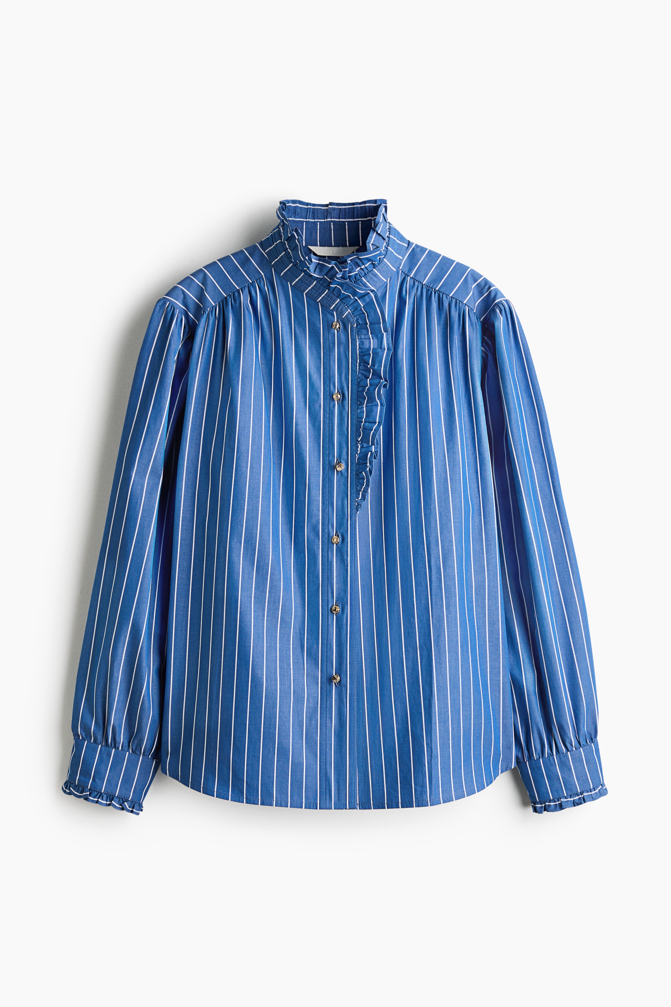 The model is wearing a blue-and-white striped long-sleeved blouse featuring a high ruffled collar and matching ruffled details along the front placket and cuffs. The blouse is tucked into high-waisted blue denim jeans, styled with a black belt featuring a large gold circular buckle.