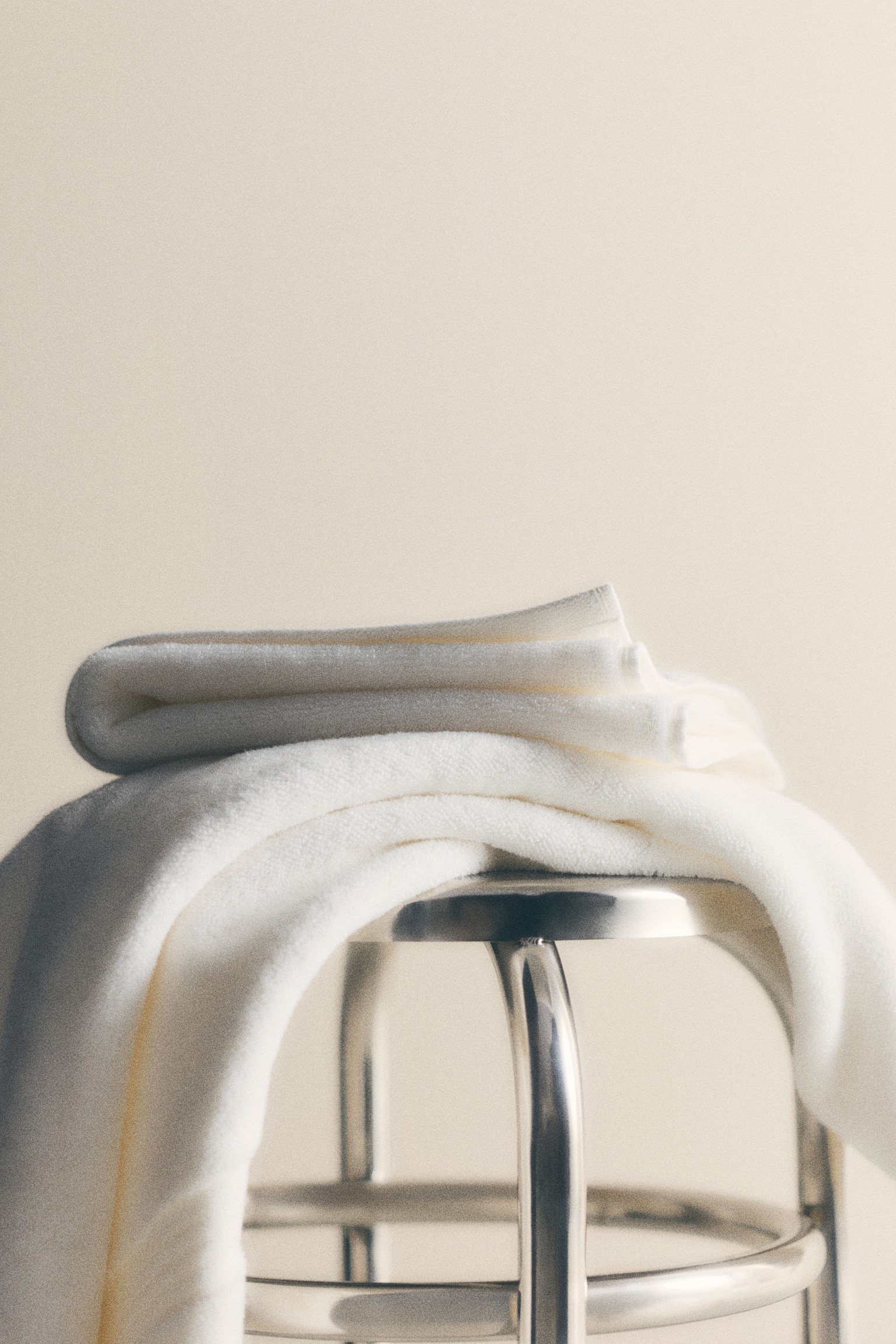 A white textured towel is hooked onto a black peg, hanging vertically. It is folded to reveal its thickness and hemmed edges, and a subtle horizontal band is visible near the bottom. - 1