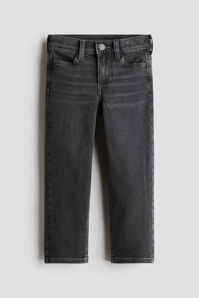A pair of dark grey slim-fit jeans is laid flat, showing the front view with a classic five-pocket design, belt loops, and a button fastening at the waist. The denim fabric shows subtle fading and whiskering across the upper thighs. - 1