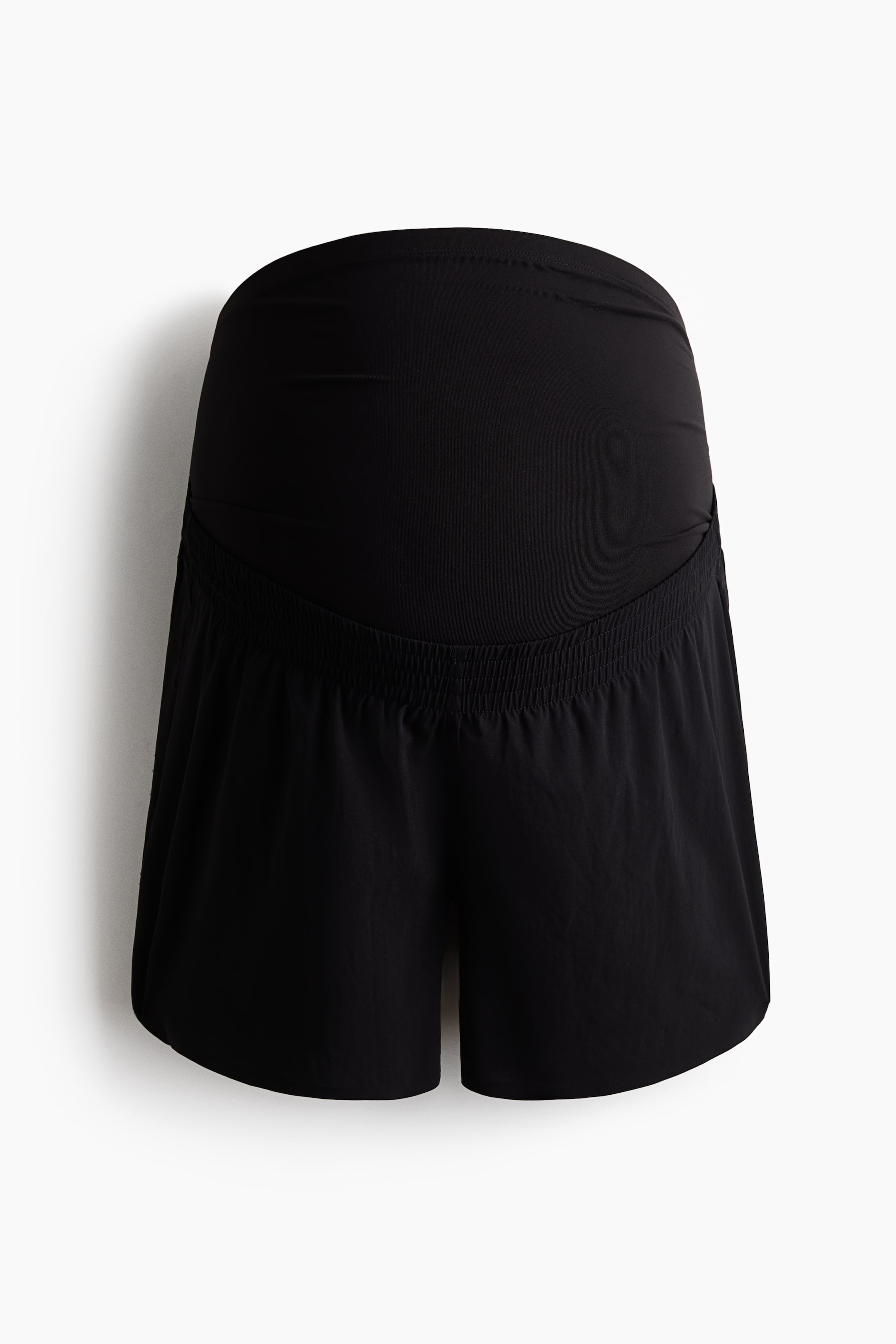 Zobacz większy obraz: Czarne szorty ciążowe mają szeroki, gładki panel zakrywający brzuch na górze, z luźniejszą dolną częścią szortów połączoną z przodu marszczonym detalem z elastycznej gumki.