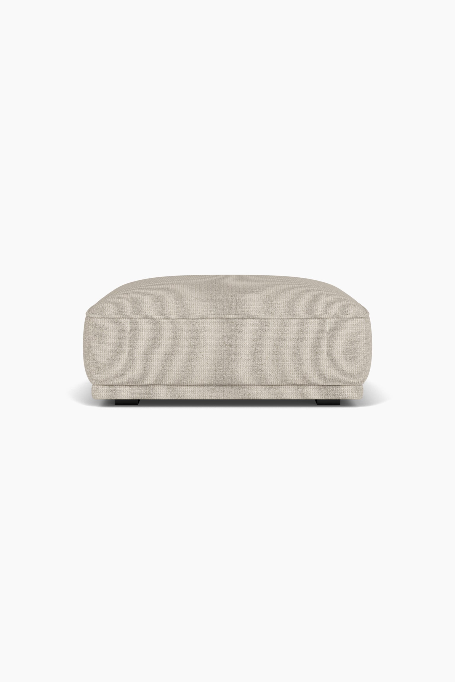 En polstret puf med et tekstureret beige stof vises forfra i en lige frontal vinkel og fremhÃ¦ver det lavprofilerede, rektangulÃ¦re design med afrundede hjÃ¸rner og kantede sÃ¸mme. MÃ¸blet hviler pÃ¥ en tilbagetrukket base med smÃ¥, mÃ¸rke blokben synlige nedenunder. - 1