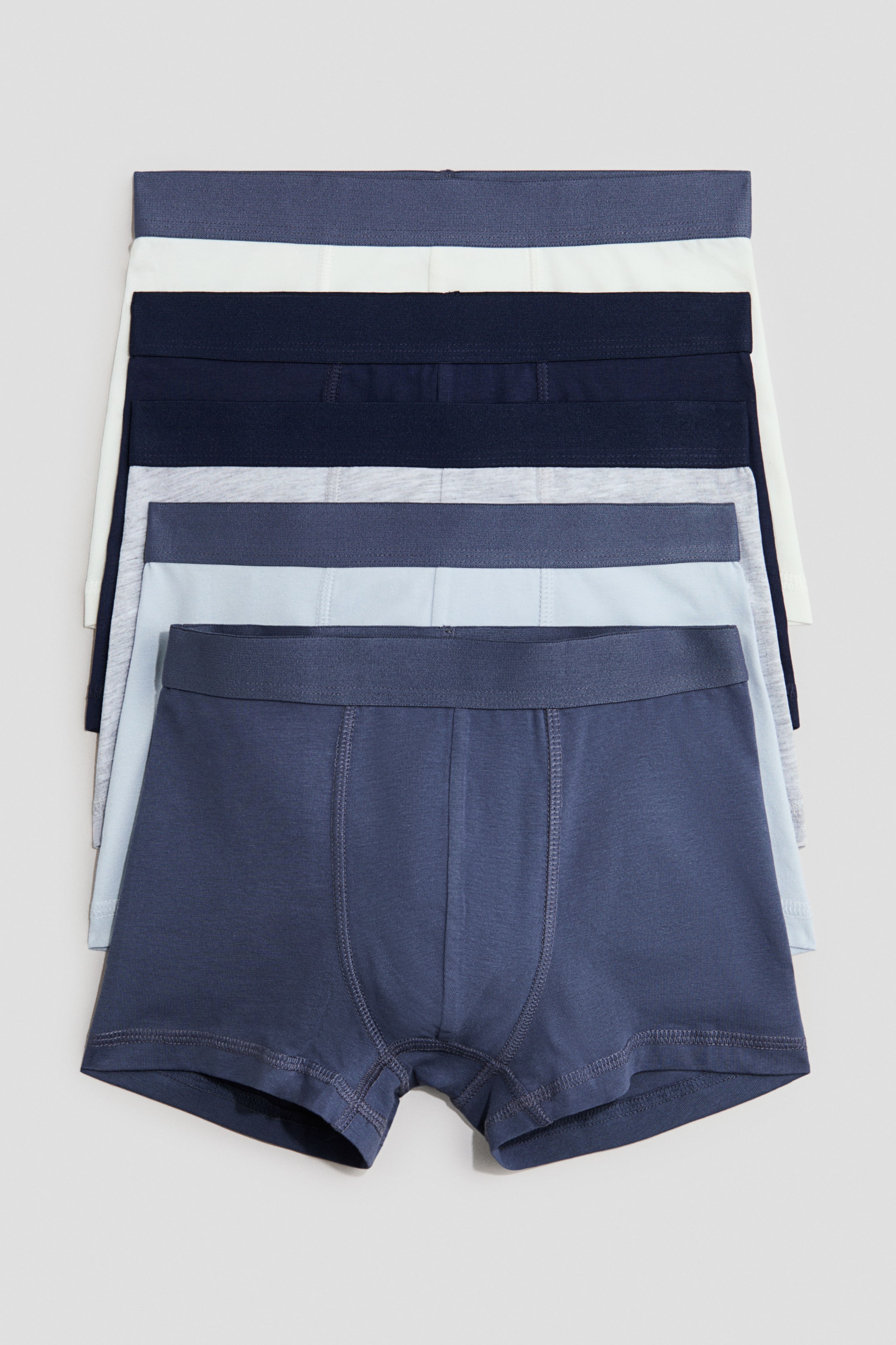 Zobacz większy obraz: Bokserki z bawełnianego dżerseju, z krótkimi nogawkami, elastycznym pasem i podszytym przodem, ułożone w stos i prezentowane z przodu. Poszczególne sztuki występują w różnych odcieniach niebieskiego, szarości i bieli, przy czym najbardziej widoczny egzemplarz wyraźnie eksponuje swoje krótkie nogawki, elastyczny pas i podszyty przedni panel.