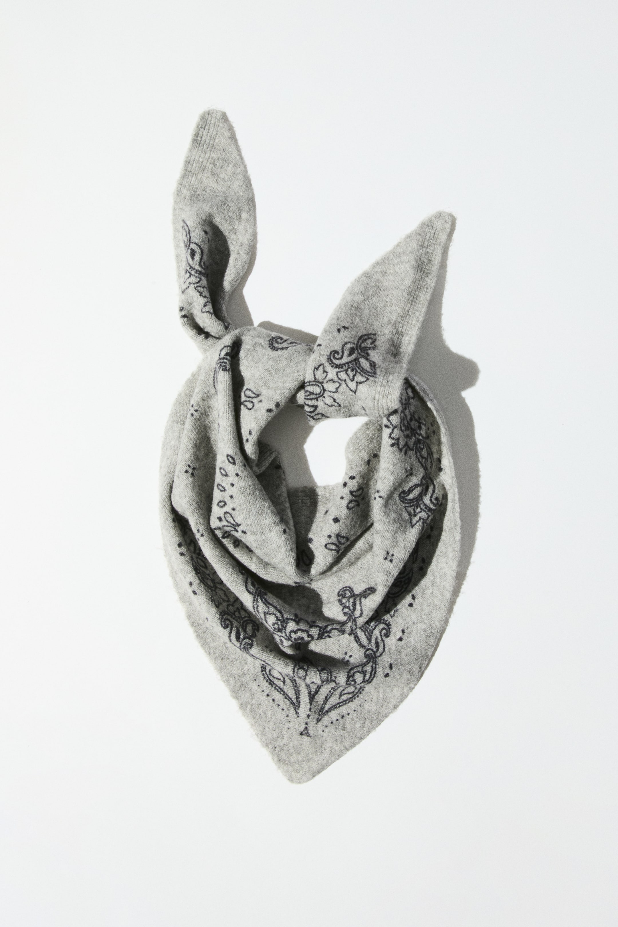 View larger image: A triangle scarf in a fine gray knit with a black paisley-style printed pattern is shown front-facing, styled in a loose loop with a knot at the top. The scarf drapes downward to a central point, showcasing the printed border design and the soft, textured fabric.