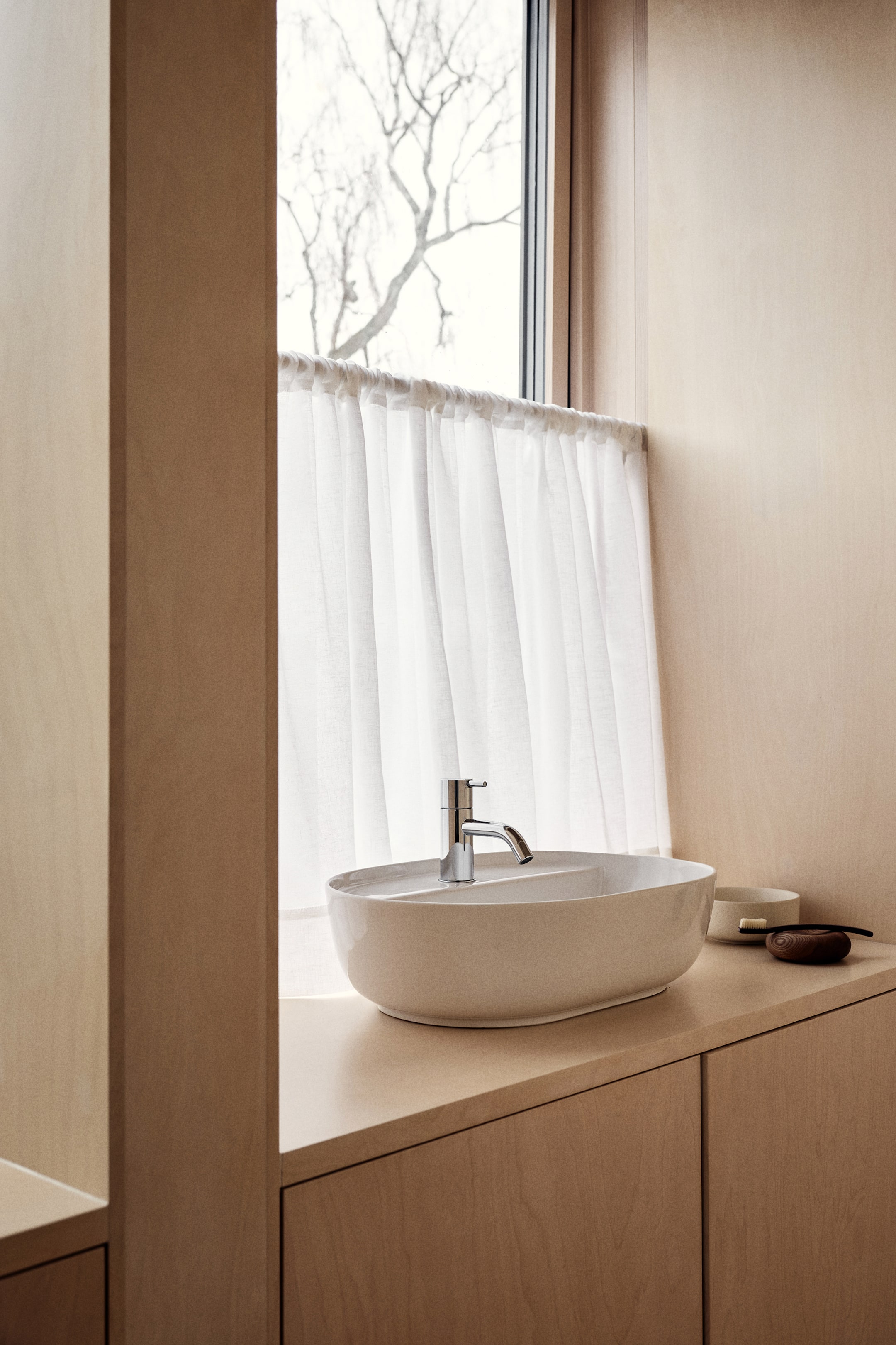 View larger image: A light beige, oval ceramic countertop basin features a chrome single-handle mixer faucet. The basin showcases a raised edge and an integrated central partition, with the faucet positioned on this partition.