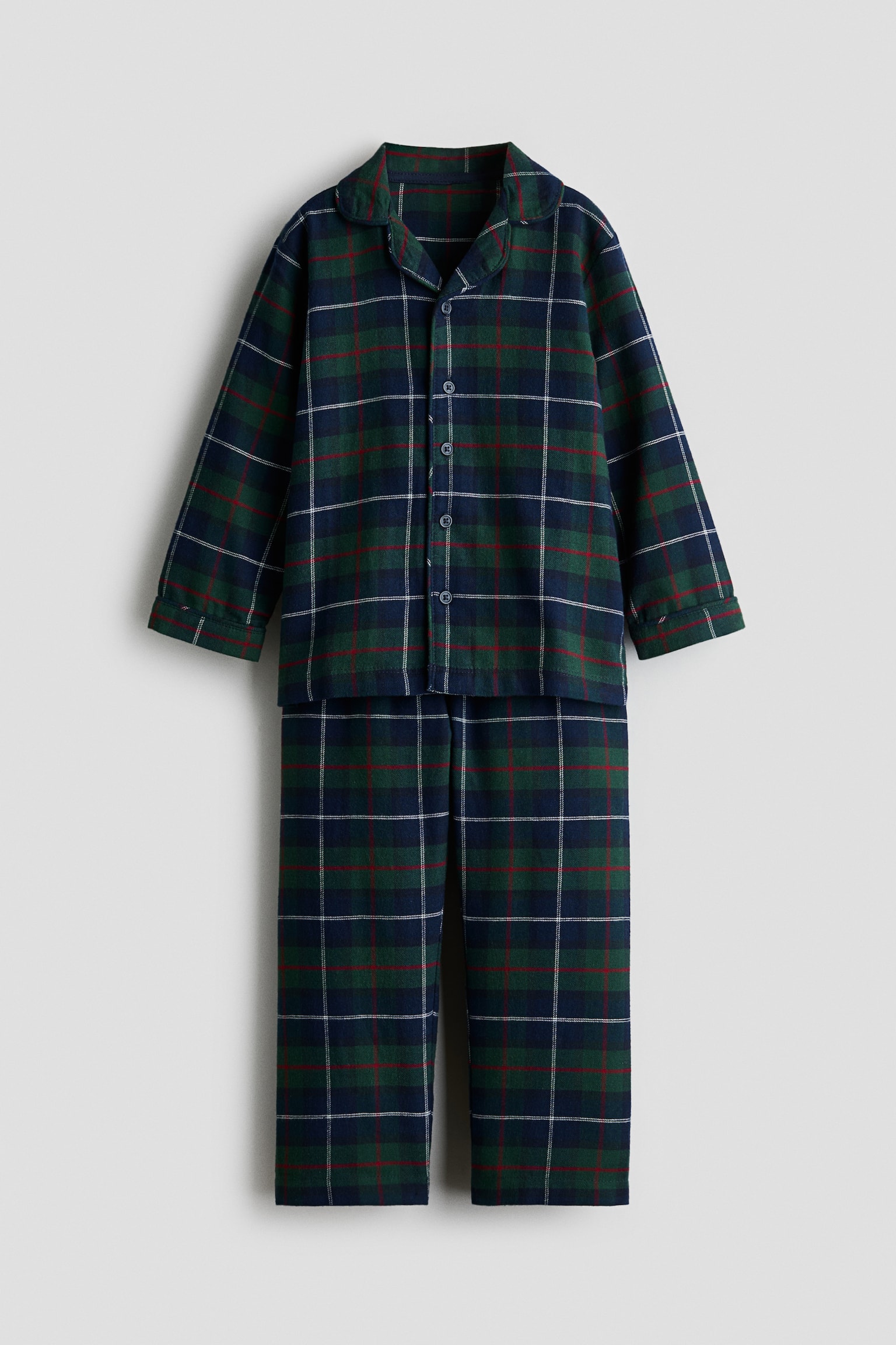 Cet ensemble de pyjama deux piÃ¨ces, vu de face, prÃ©sente un motif tartan Ã  carreaux vert et bleu marine avec de fines lignes blanches et rouges croisÃ©es. Le haut Ã  manches longues affiche un col Ã  revers arrondi et une fermeture boutonnÃ©e sur le devant, tandis que le pantalon assorti Ã  jambe droite est suspendu juste en dessous.