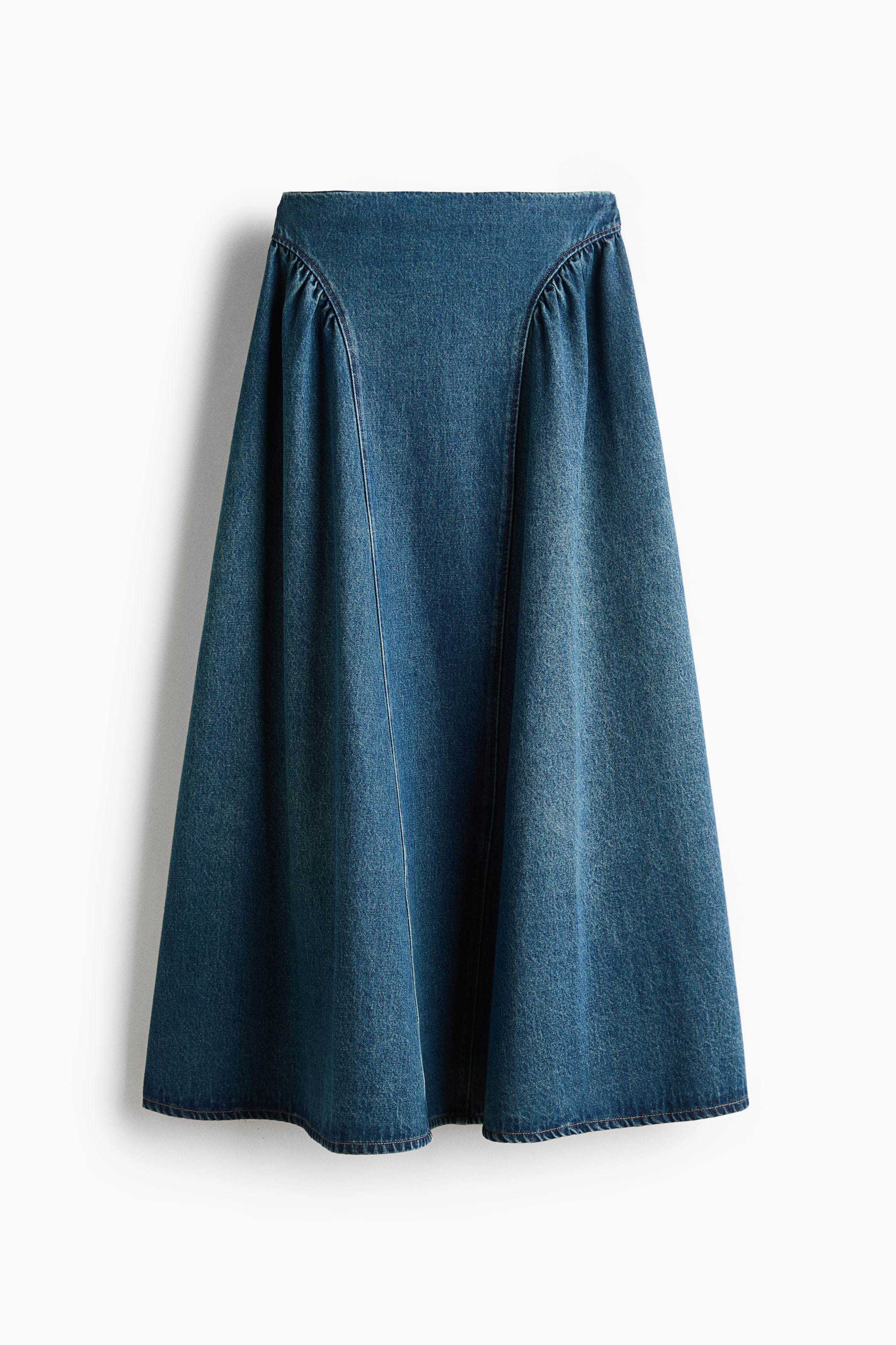View larger image: A blue denim A-line skirt is hanging, shown from the front. It features a flat waistband with subtle gathers below it and prominent vertical seams.