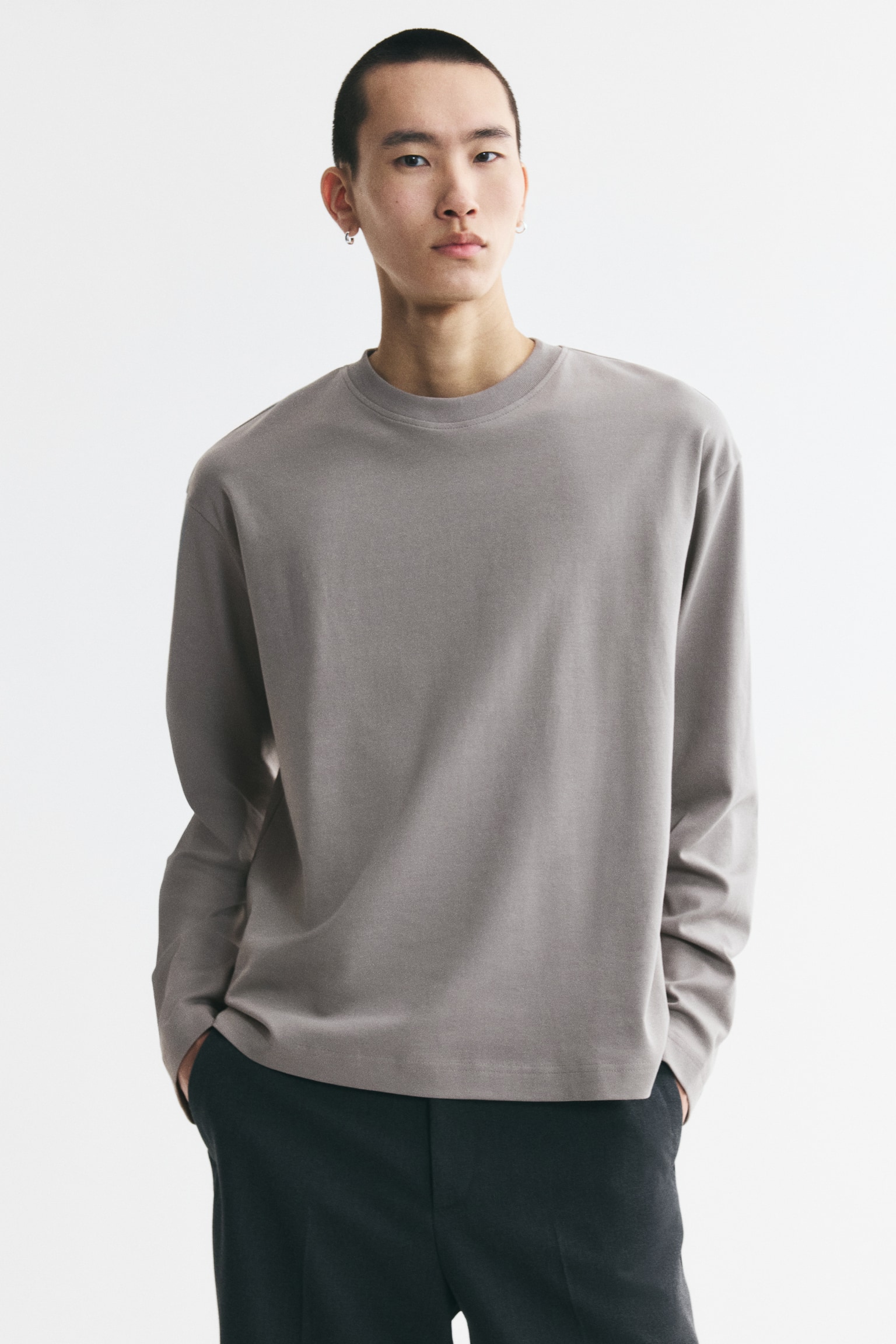 A taupe long-sleeved t-shirt is laid flat, featuring a crew neck, dropped shoulders, wide sleeves, and a straight hem. - 1