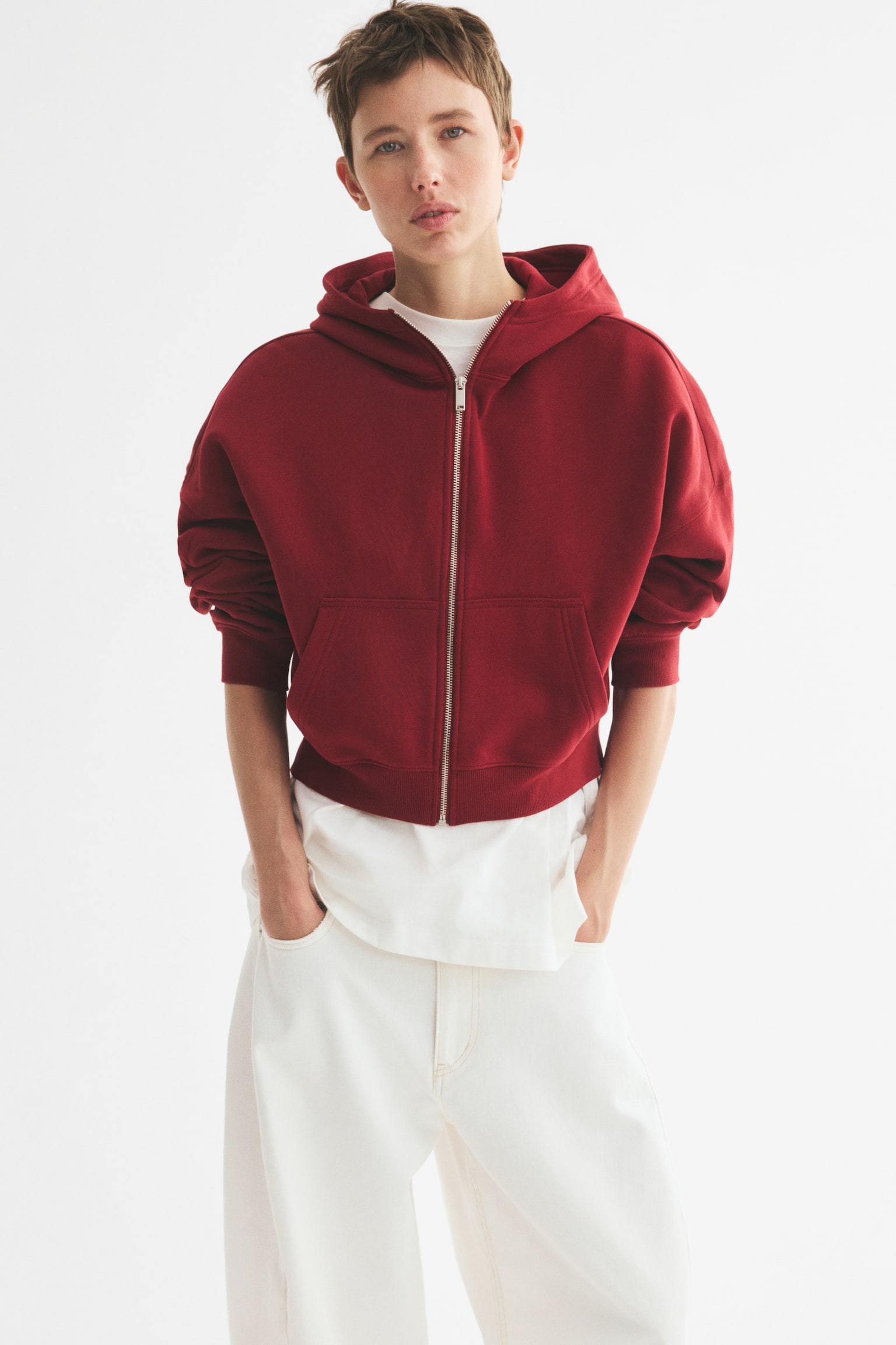 A relaxed-fit red hoodie crafted from sweatshirt fabric is displayed from the front, showcasing a lined hood, a silver zip down the front, and patch pockets at the front. It also features dropped shoulders, long sleeves with ribbed cuffs, and a ribbed hem. - 1