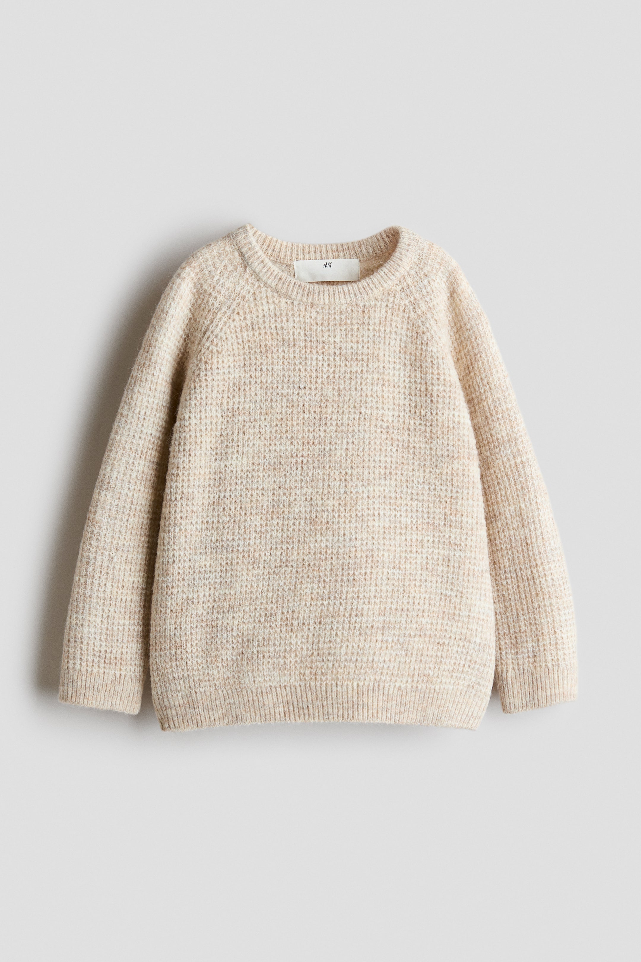 Agrandir l'image: Un pull en maille texturée chinée beige est posé à plat, face avant visible. Il présente un col rond, des manches raglan, ainsi que des poignets et un bas côtelés, avec une étiquette blanche « H&M » visible à l’arrière du col.