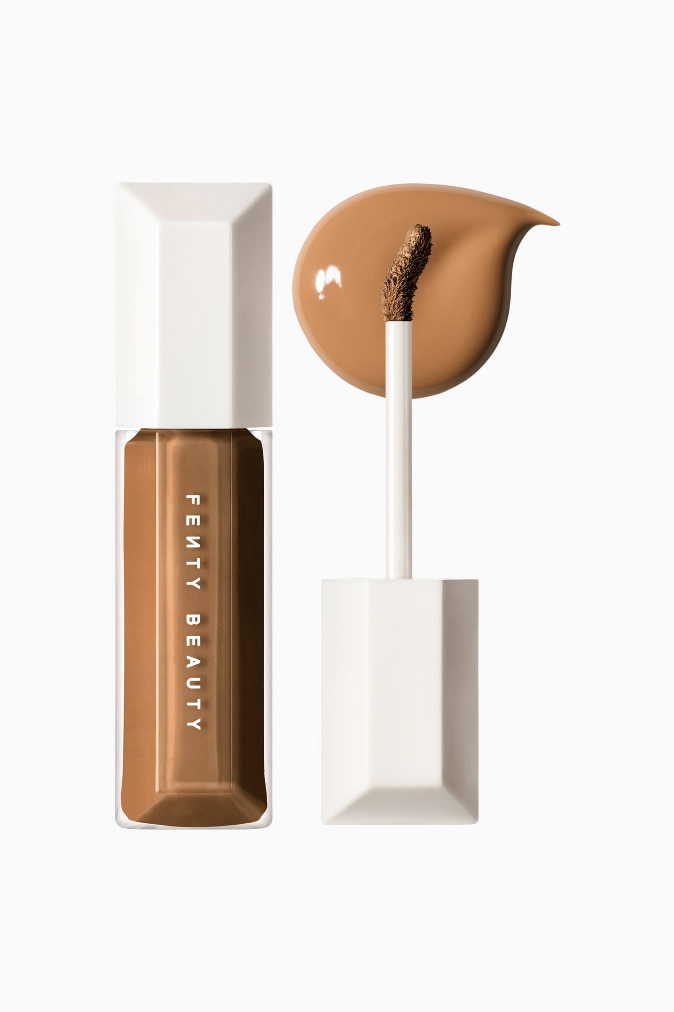 Visa större bild: We're Even Hydrating Longwear Concealer står upprätt i en klar, sexkantig flaska fylld med en medelmörk till mörkbrun vätska och toppad med ett vitt facetterat korklock. Bredvid flaskan visar en uppskruvad applikatorstav en böjd, produktbelagd spets placerad ovanför en jämn, glansig, droppformad färgprovning av concealern.