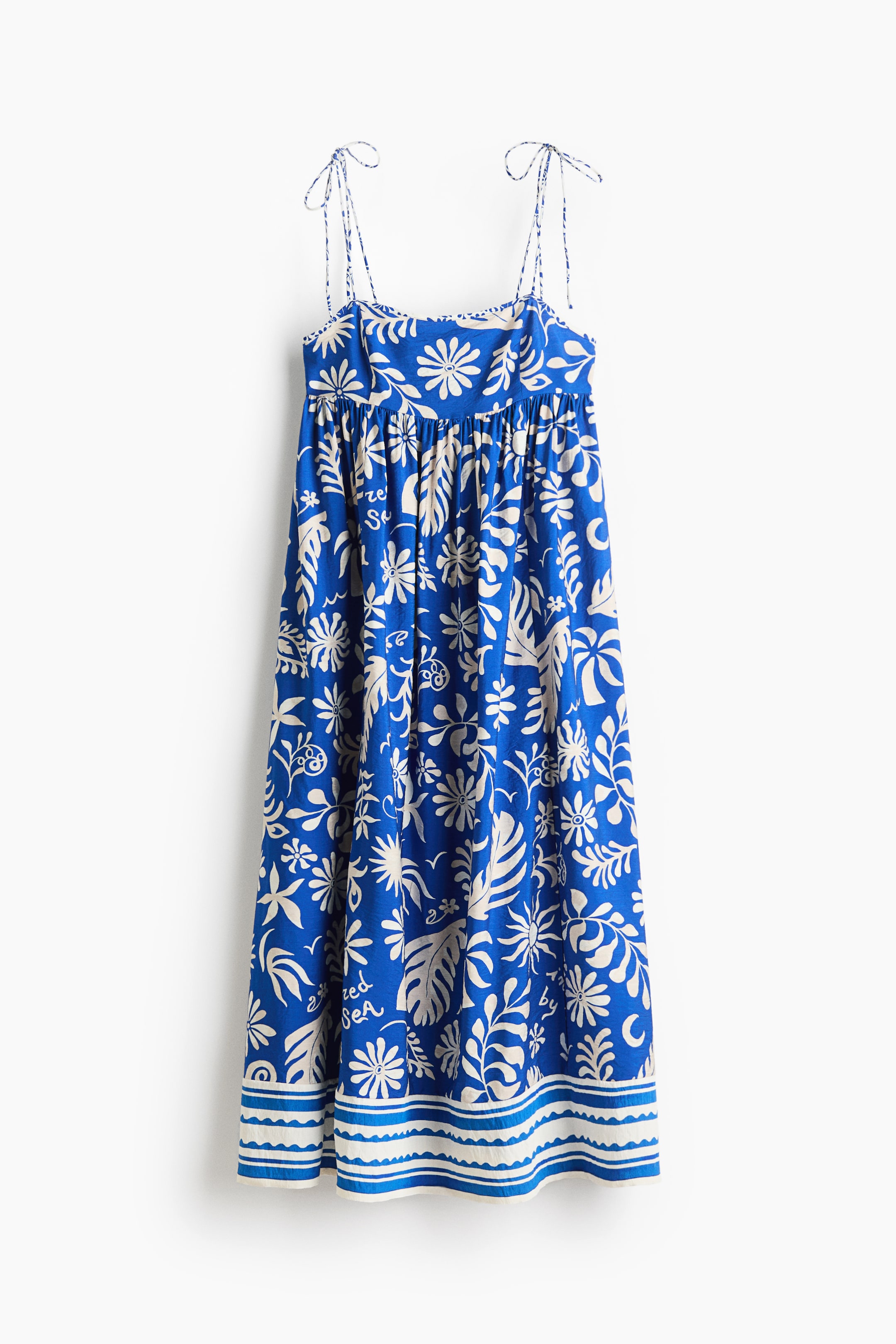 View larger image: A calf-length dress is showcased front-facing, crafted from a blue viscose-blend weave adorned with an all-over off-white floral and leaf motif, complemented by a decorative striped border at the hem. It features a square neckline, tie-top spaghetti shoulder straps, a slim-fit section over the bust, and gathers that add volume to the skirt.