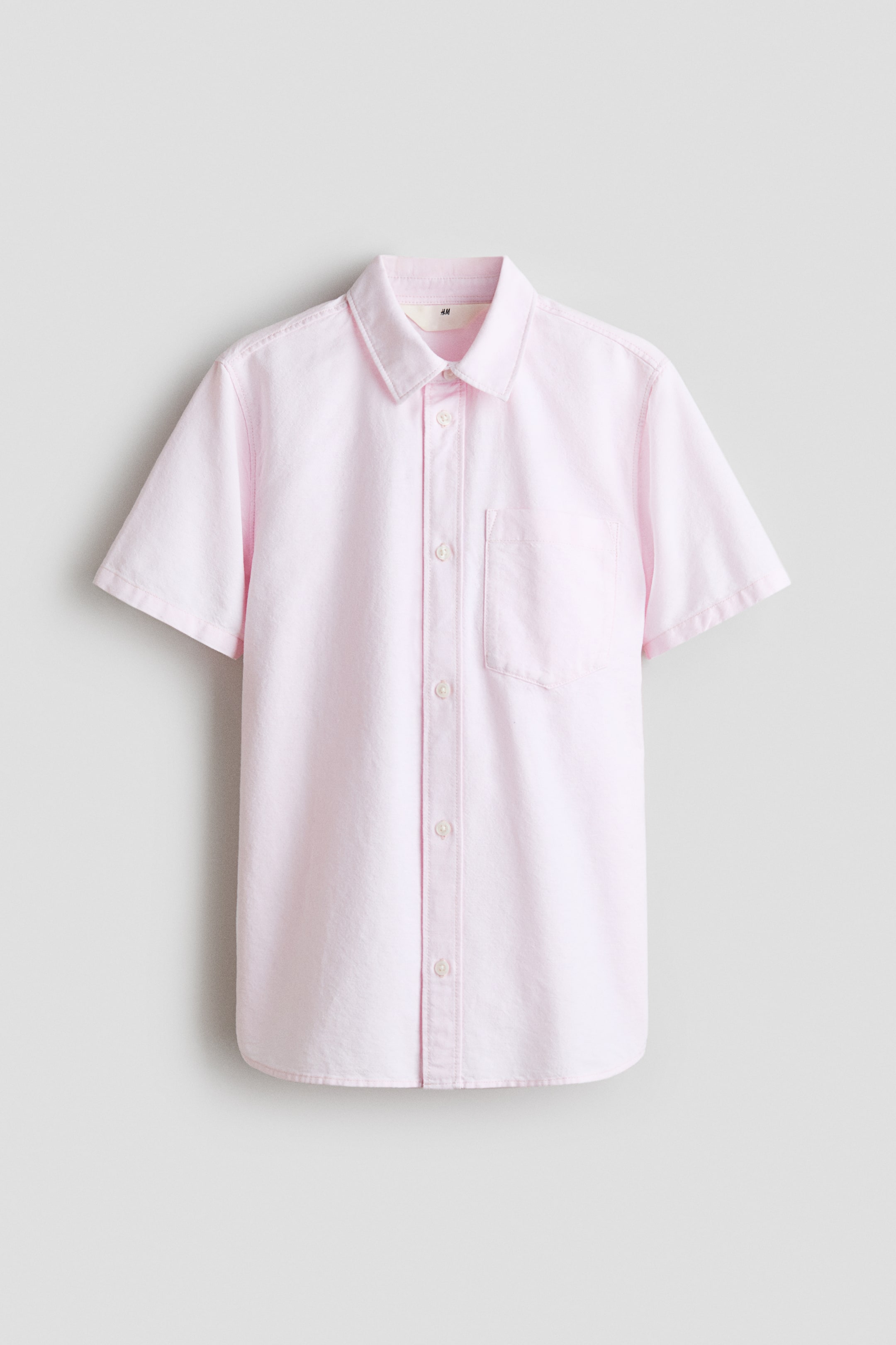 View larger image: A pink short-sleeved shirt is showcasing its front view, featuring a cotton weave, a turn-down collar, buttons running down the front, a chest pocket on the left side, and a gently rounded hem.