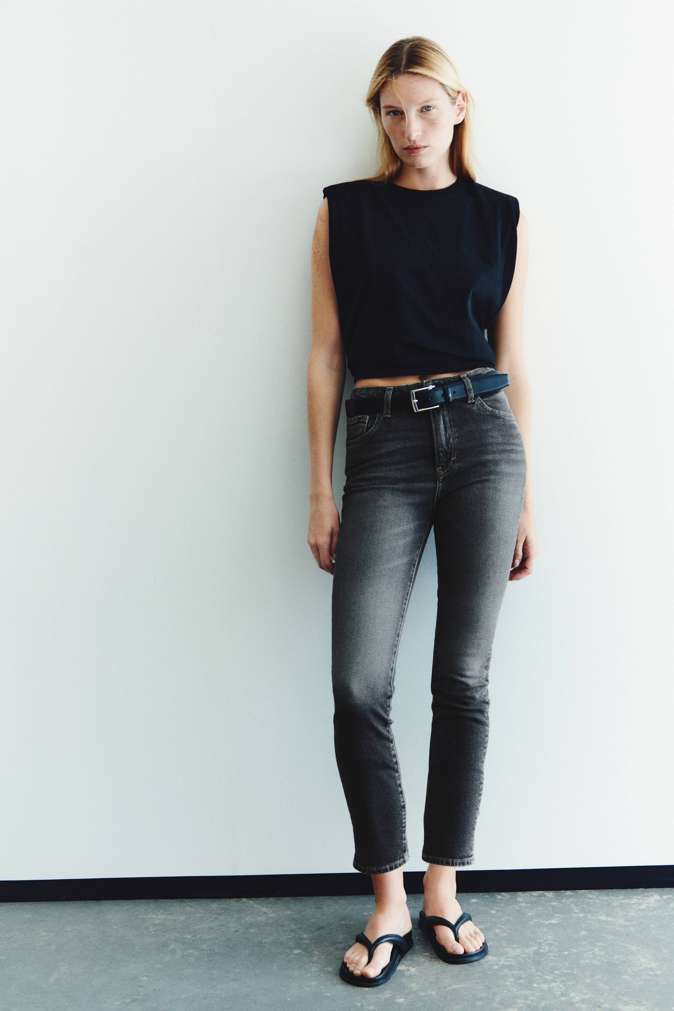 View larger image: These high-waisted, slim-fit jeans in washed dark gray denim are worn by the model and feature a straight-leg cut that ends at the ankle. The jeans are styled with a black leather belt, a sleeveless black crop top, and black thong sandals.