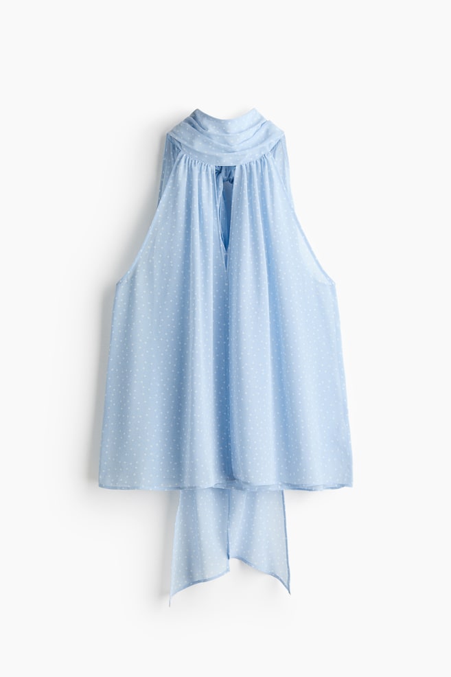 Una blusa azul claro de corte holgado se muestra desde atrás, confeccionada en un tejido transparente y arrugado con pequeños puntos blancos. Está diseñada con un corte estrecho en la parte superior, un cuello de bufanda fruncido y una abertura en forma de V en la espalda, con las cintas de la bufanda extendiéndose hacia abajo. - 1