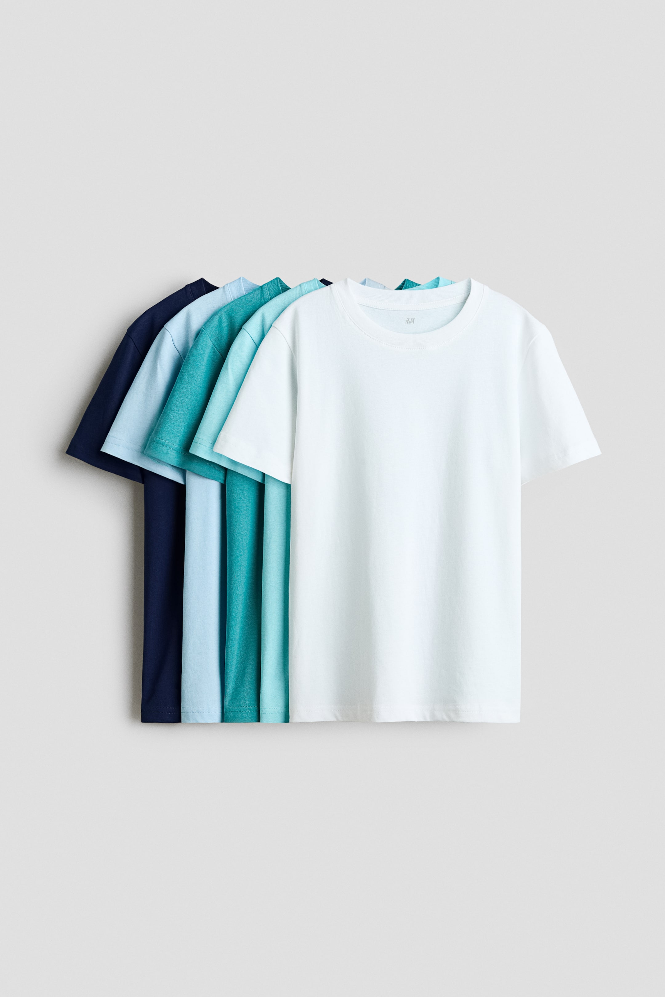 View larger image: Five T-shirts in soft cotton jersey are fanned out in a gradient of blue and white tones, each featuring a crew neck and a straight hem, with the front of the white T-shirt fully visible.