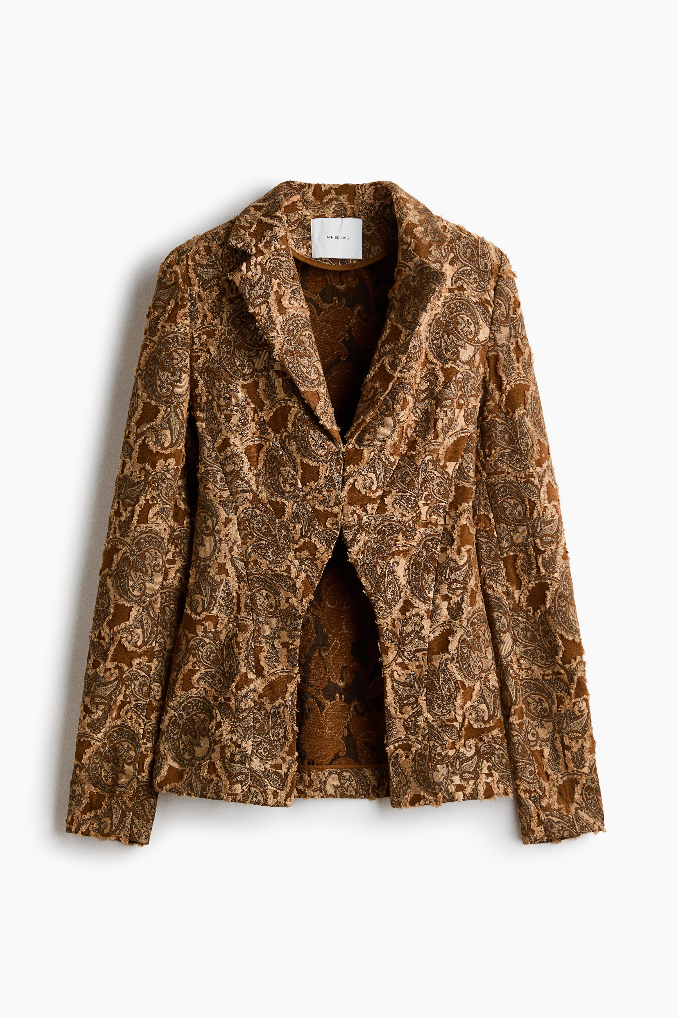 Má»t chiáº¿c blazer má»t hÃ ng khuy báº±ng váº£i jacquard dá»t ná»i mÃ u nÃ¢u vÃ ng vá»i há»a tiáº¿t paisley vÃ  ve Ã¡o notch Äang ÄÆ°á»£c ngÆ°á»i máº«u máº·c má». Blazer ÄÆ°á»£c phá»i cÃ¹ng Ã¡o á»ng Äá»ng bá» bÃªn trong vÃ  quáº§n mÃ u xanh Ã´ liu.