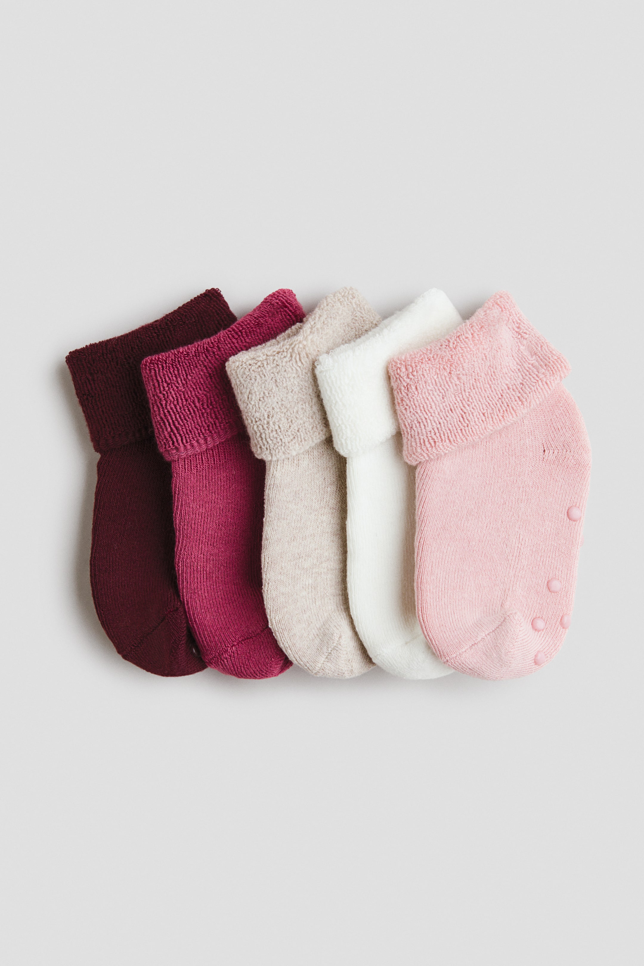 Agrandir l'image: Un lot de cinq chaussettes est présenté en bordeaux, magenta, beige, blanc cassé et rose clair. Chaque chaussette est dotée d’un corps en maille fine et d’une tige repliable, avec un revers intérieur présentant une texture éponge visible. La chaussette rose clair montre également des protections antidérapantes circulaires sur sa semelle.