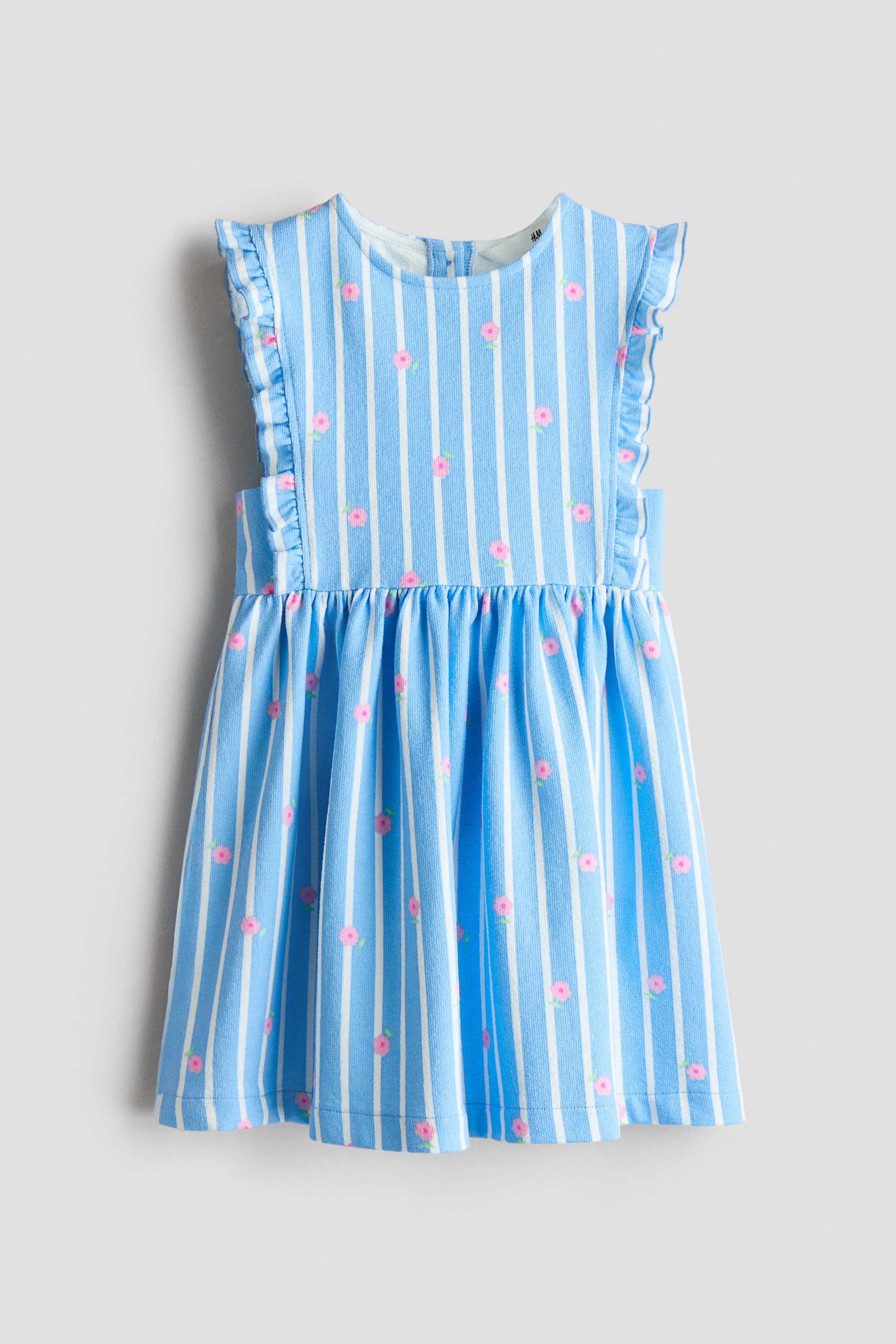 Προβολή μεγαλύτερης εικόνας: Ένα φόρεμα χωρίς μανίκια από υφασμάτινο βαμβακερό ζέρσεϊ, με μπλε και λευκές ρίγες διακοσμημένες με μικρά ροζ λουλουδάτα μοτίβα. Διαθέτει φριλ διακοσμήσεις κατά μήκος των οπών των χεριών, στρογγυλή λαιμόκοψη, πιέτες στη μέση και φούστα σε γραμμή Α.