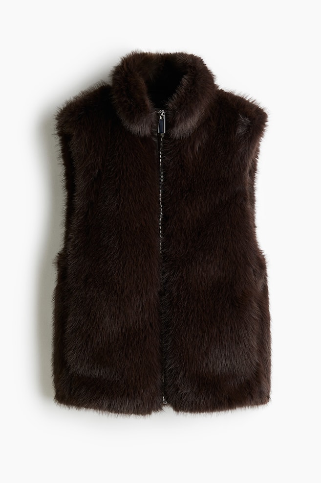 A dark brown gilet is presenting its FRONT, featuring a soft, fluffy, fur-like texture. It is designed with a stand collar and a full-length central front zip, which is set into a coated panel, showcasing a voluminous, slightly puffy silhouette towards its hem. - 1