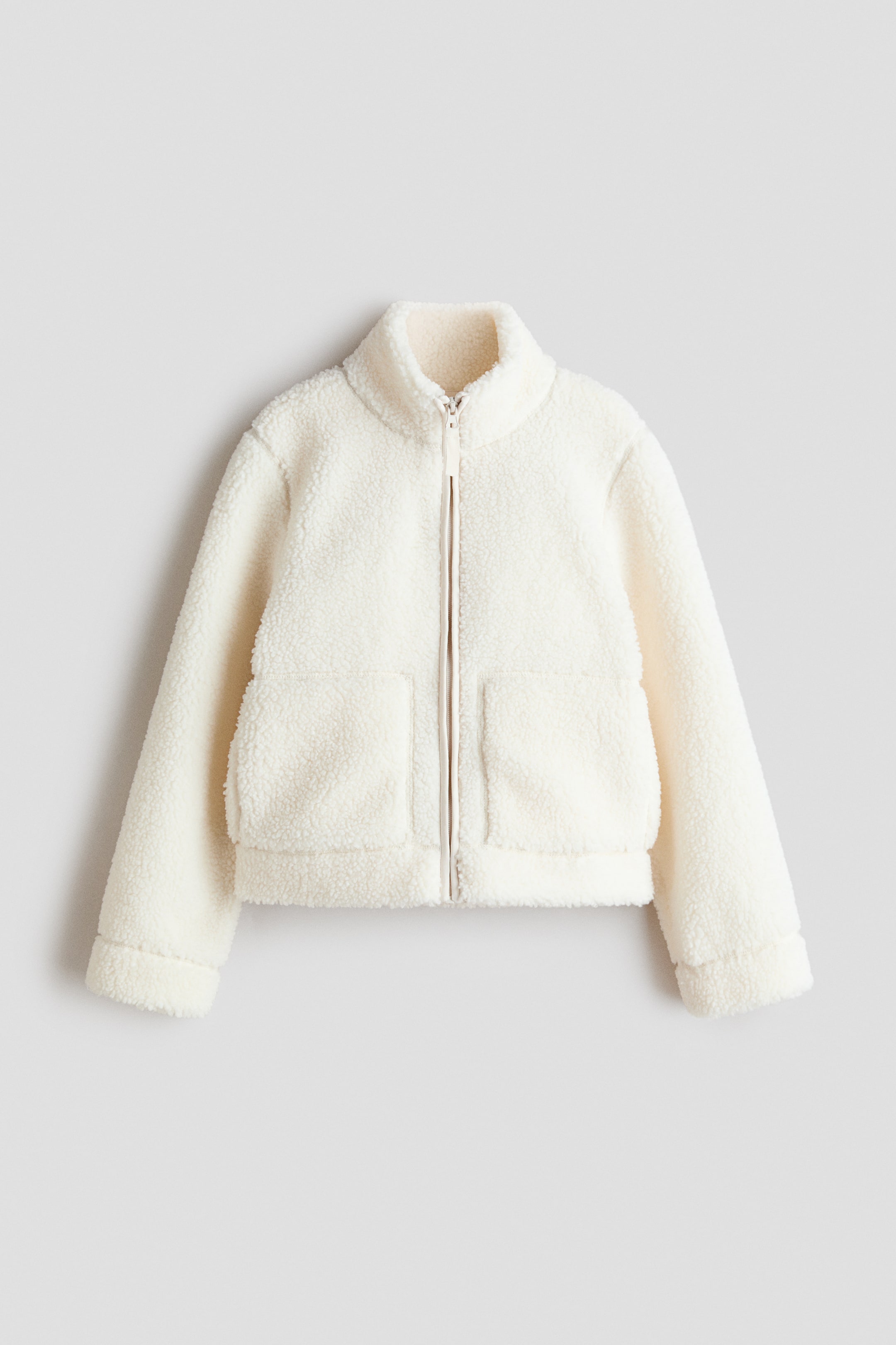 View larger image: A cream-coloured sherpa jacket is facing front, featuring a full-zip closure, a stand-up collar, two large patch pockets on the lower front, long sleeves with folded cuffs, and a straight hem.