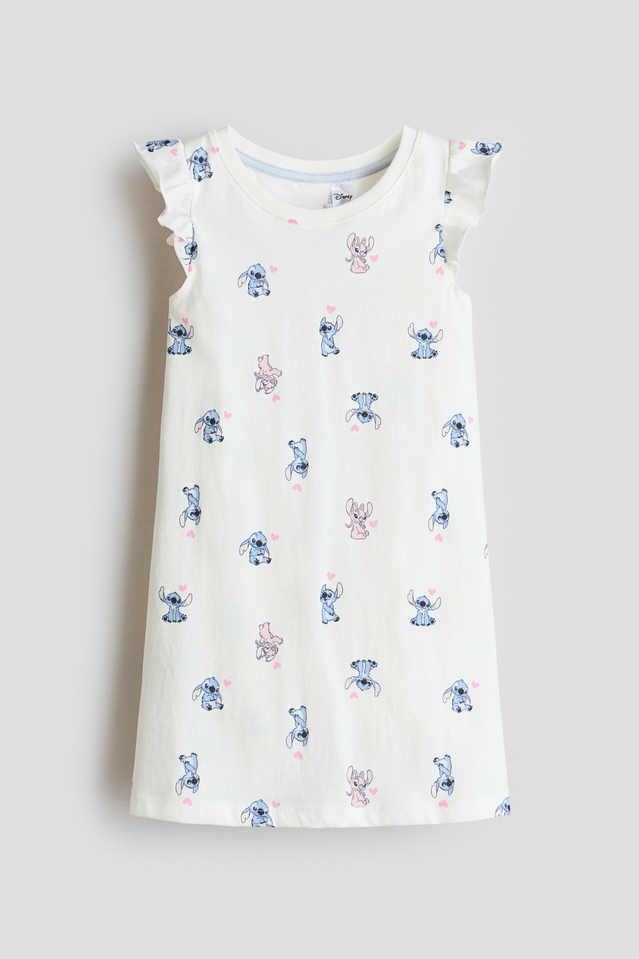 View larger image: The nightdress is displayed from the front, crafted from soft, cream-coloured cotton jersey. It features a round neckline and charming ruffled flutter sleeves. The fabric is adorned with an all-over print of blue and pink cartoon characters, interspersed with small pink hearts, and is tailored in a relaxed, straight fit.