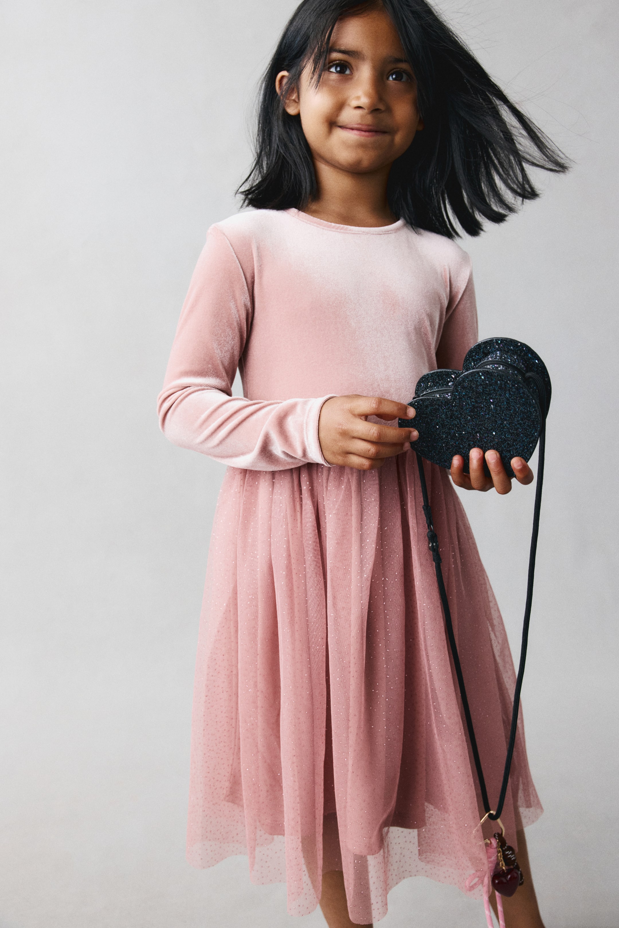 View larger image: A model is wearing a front-facing, long-sleeved pink dress featuring a soft velour bodice with a round neckline and a voluminous, gathered tulle skirt with fine glitter.