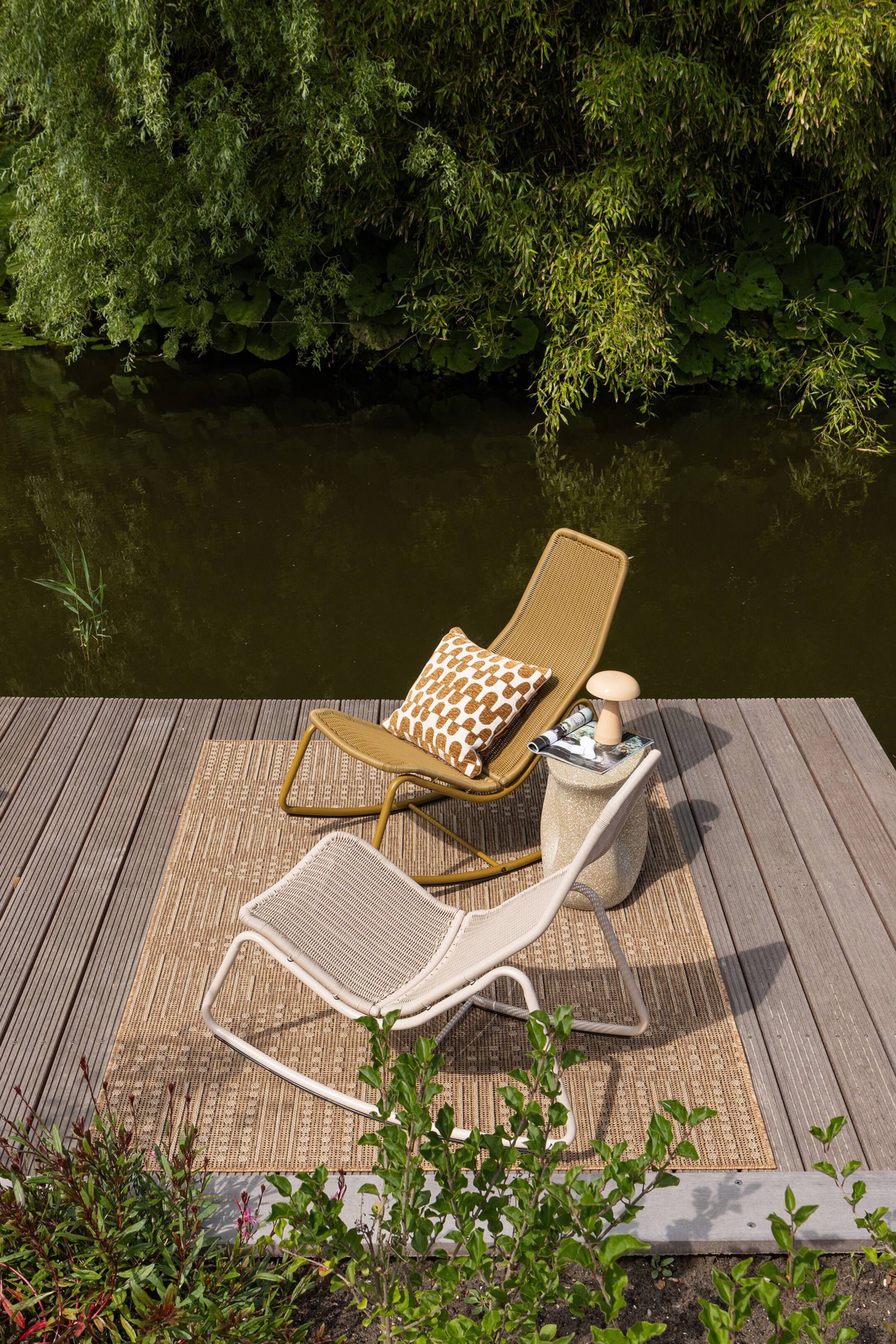 Agrandir l'image: Un tapis rectangulaire d'extérieur présente une texture tissée en brun clair et beige avec un motif géométrique répétitif. Deux chaises reposent sur sa surface.