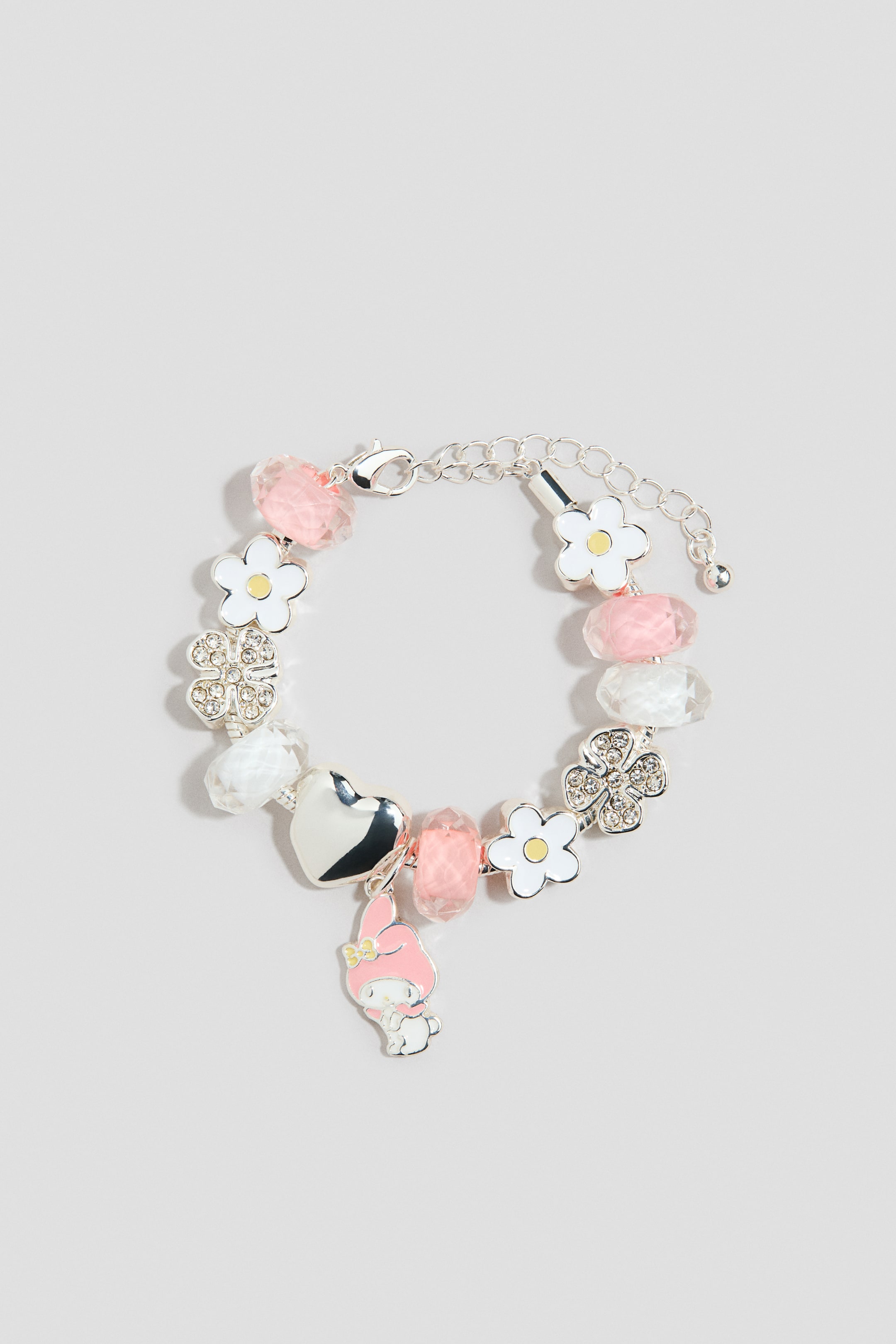 Voir une image plus grande: Un bracelet breloque ton argenté présente sa face AVANT, doté d’un fermoir mousqueton et d’une chaîne d’extension. Le bracelet est orné de perles facettées transparentes et roses, de fleurs en émail blanc aux centres jaunes, d’un trèfle à quatre feuilles ton argenté orné de strass, d’un cœur ton argenté et d’une breloque représentant un personnage en émail rose et blanc.