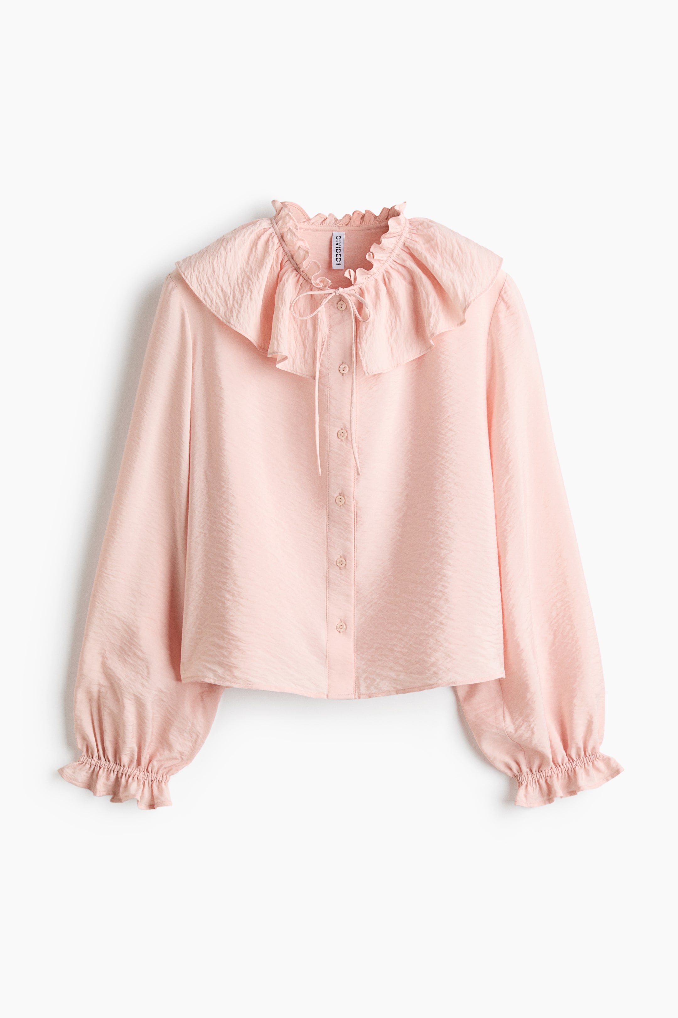 Agrandir l'image: Une blouse rose est présentée de FACE, mettant en avant un tissu subtilement texturé, un col à volants avec un cordon de serrage étroit, et un large volant autour de l'encolure. Elle arbore des boutons qui descendent le long du devant, et des manches longues et volumineuses avec une élastication étroite et un bord à volants aux poignets.