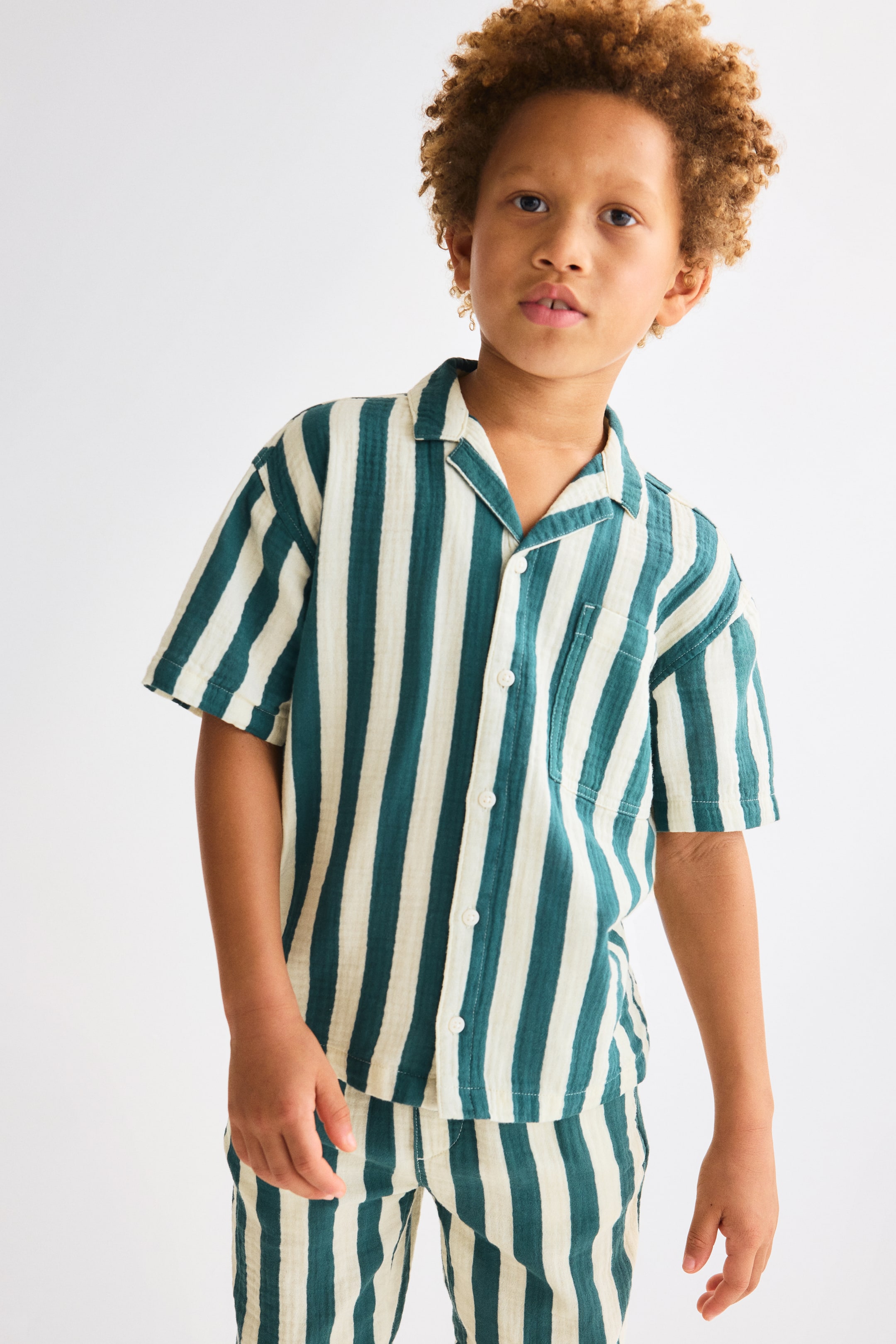 Agrandir l'image: Vue de face d'une chemise de villégiature à manches courtes et d'un ensemble de shorts assortis, avec des rayures verticales en bleu canard foncé et crème. La chemise est conçue avec un col de villégiature, des boutons à l'avant et une poche poitrine appliquée.