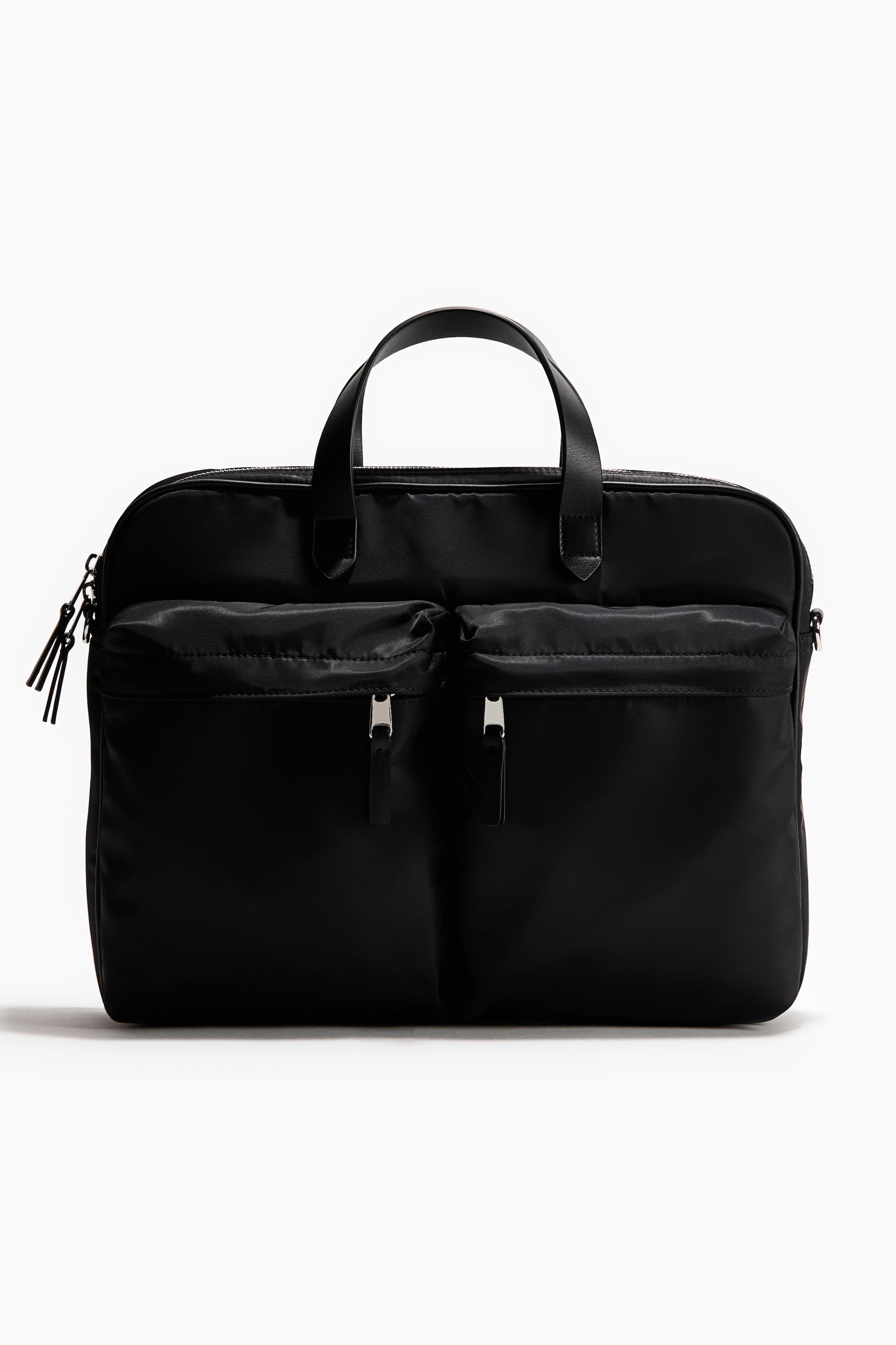 Ampliar la imagen: Un maletín negro de nylon presenta su frente, con dos asas superiores de cuero sintético negro y un compartimento principal con cierre en la parte superior. Dos bolsillos grandes con cierre de cremallera están visibles en el frente, cada uno con un tirador plateado y una lengüeta negra, mientras que un cierre lateral con múltiples tiradores aparece a la izquierda.