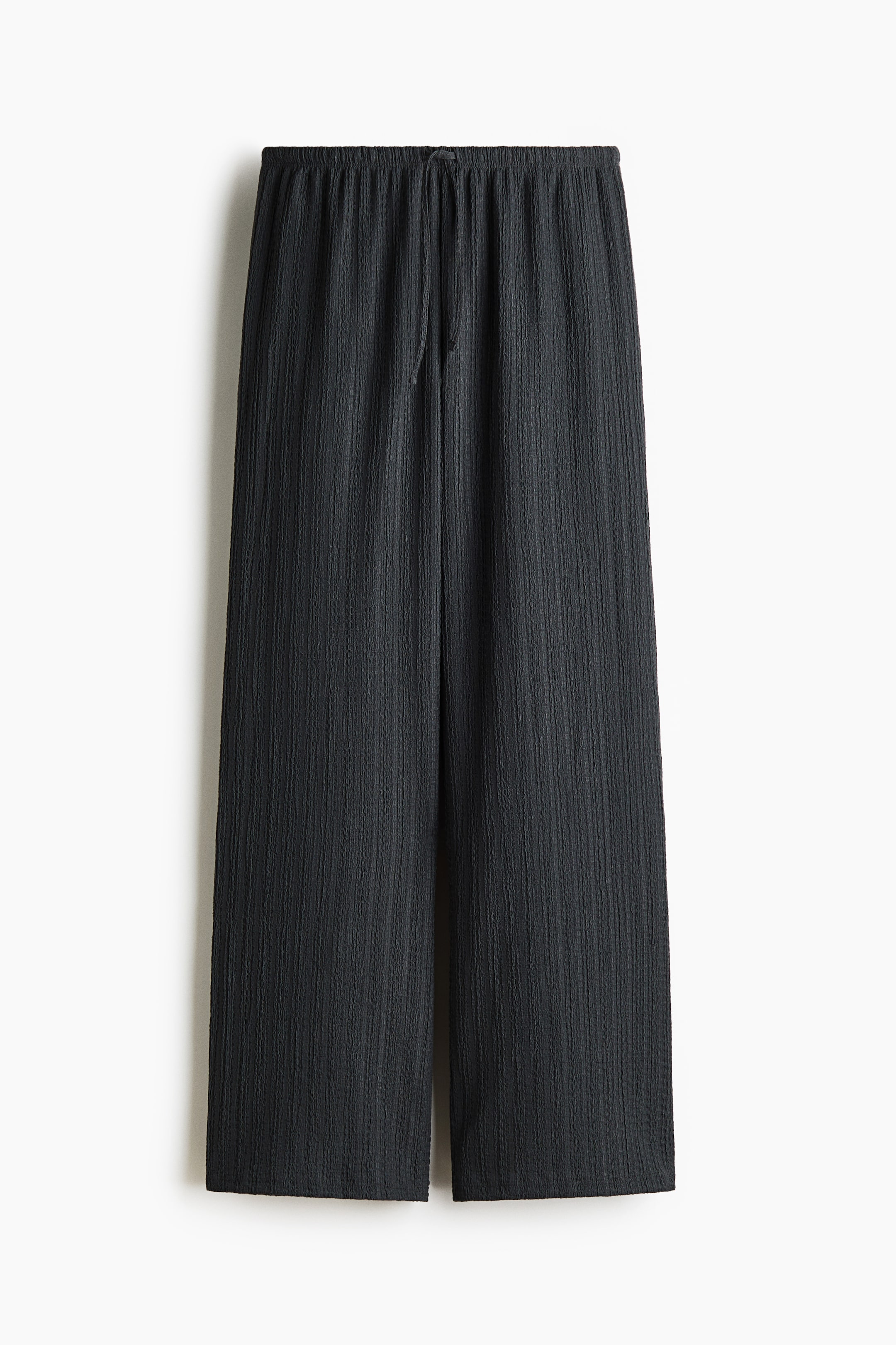 View larger image: The front of the dark gray pants is featuring a vertical ribbed texture. They are showcasing an elasticized waistband with a visible central drawstring tie and are cut in a wide-leg, relaxed fit.