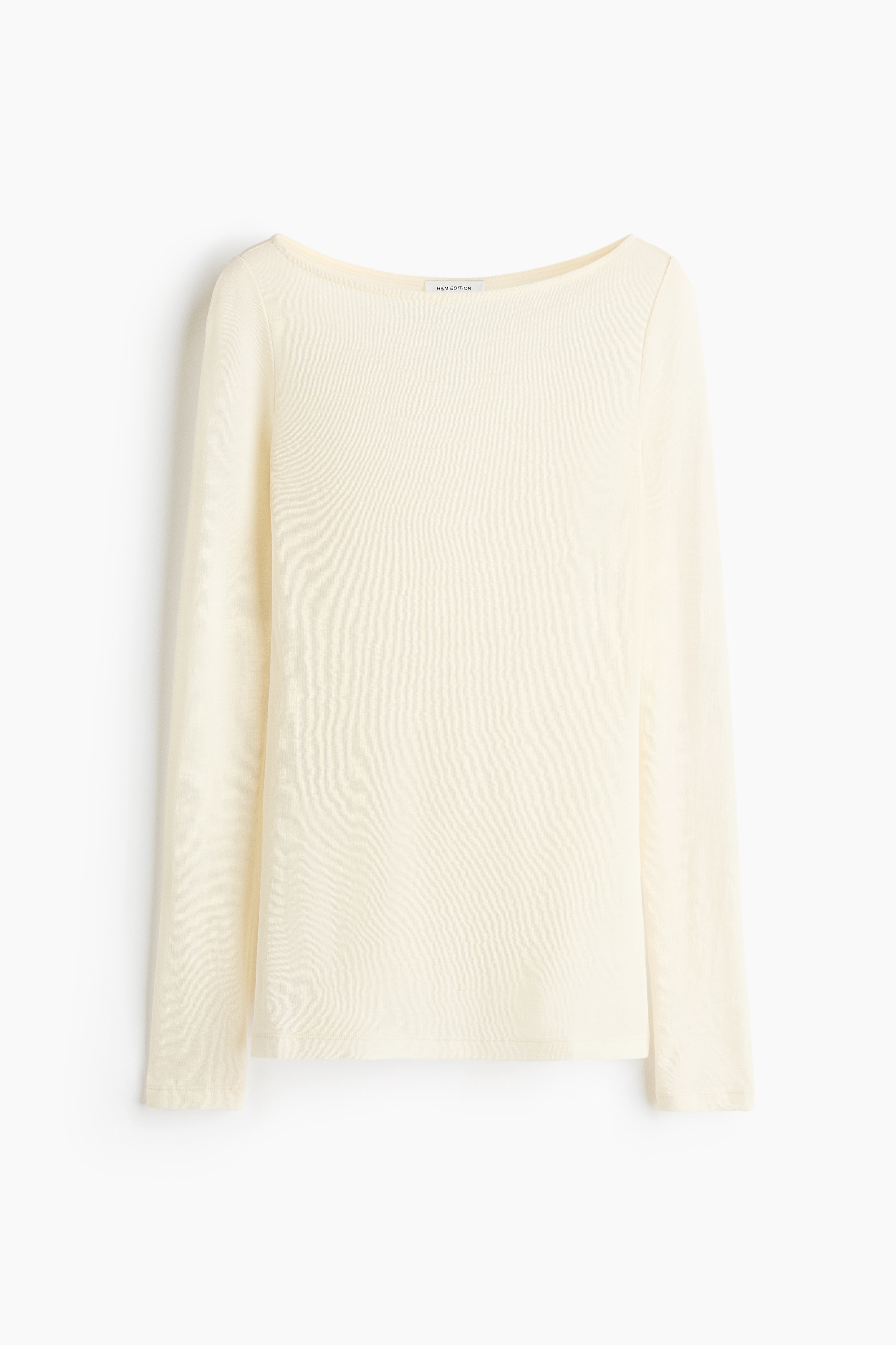This cream-coloured rib-knit wool top with a boat neck and long sleeves is worn by the model. The semi-sheer top is layered over a dark undergarment and paired with black leather pants.